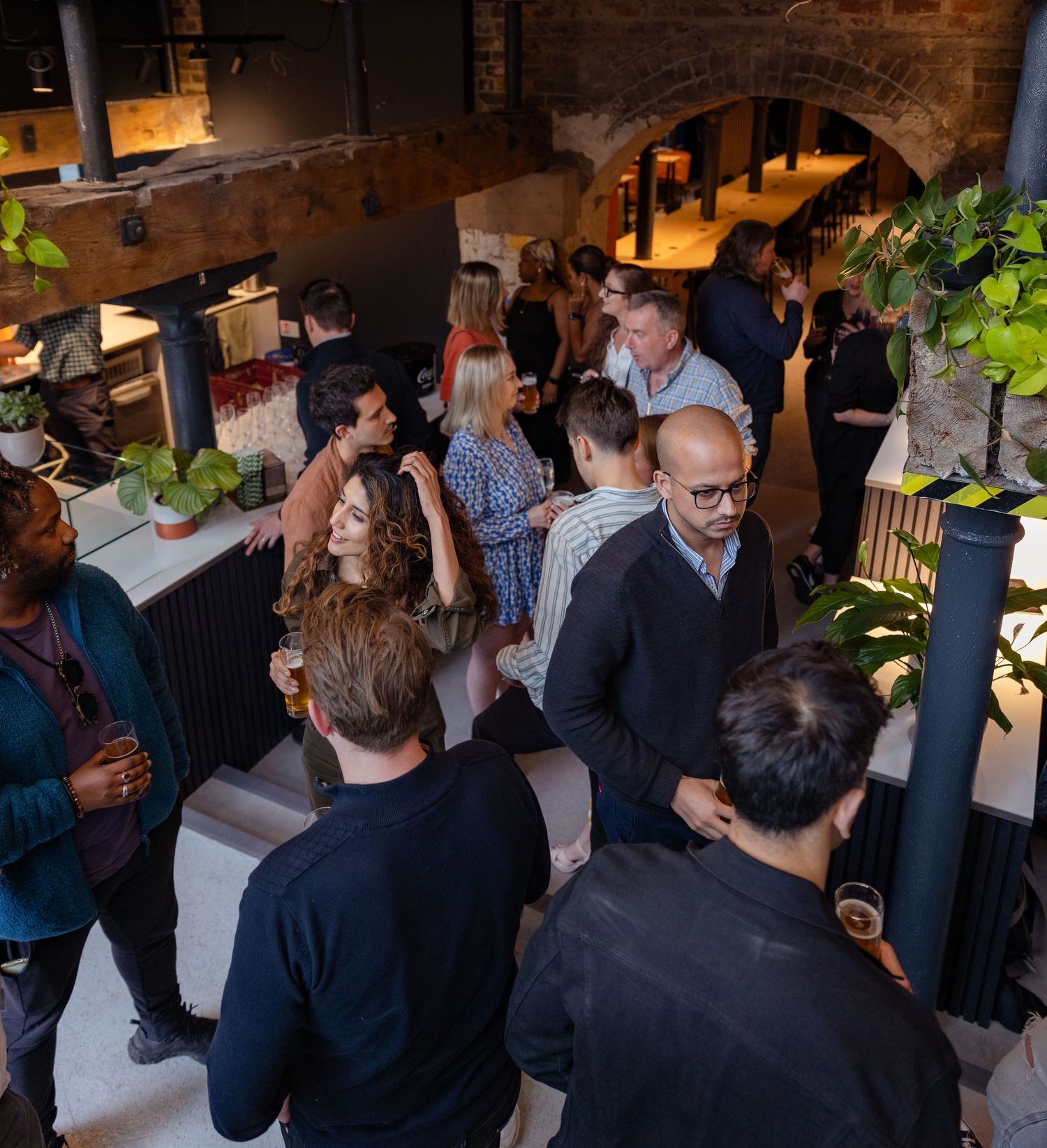 Guests mingling at a stylish indoor networking event with plants and warm lighting.