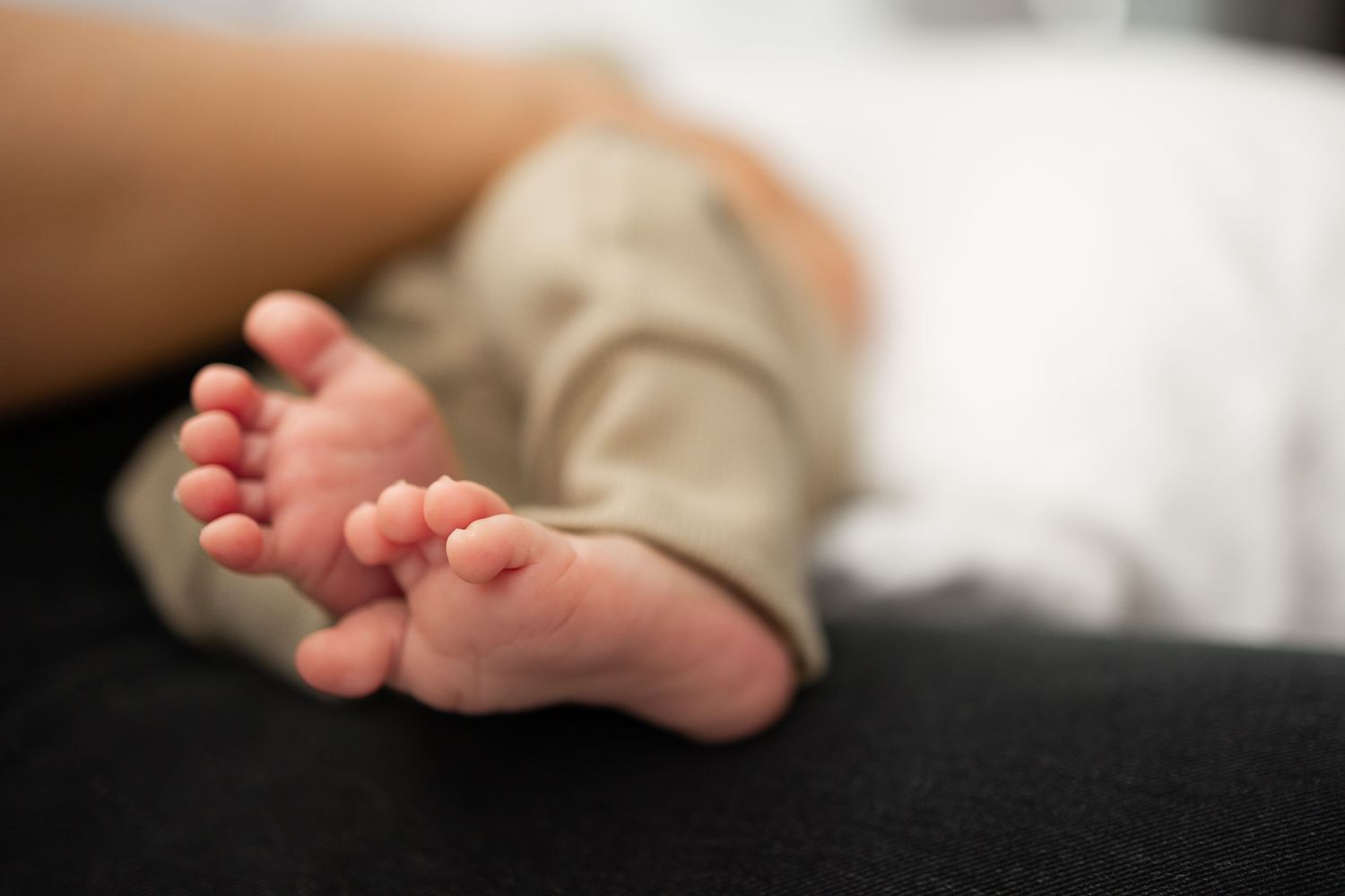 Close-up of tiny newborn baby feet resting on a dark surface, wearing loose gray pants.
