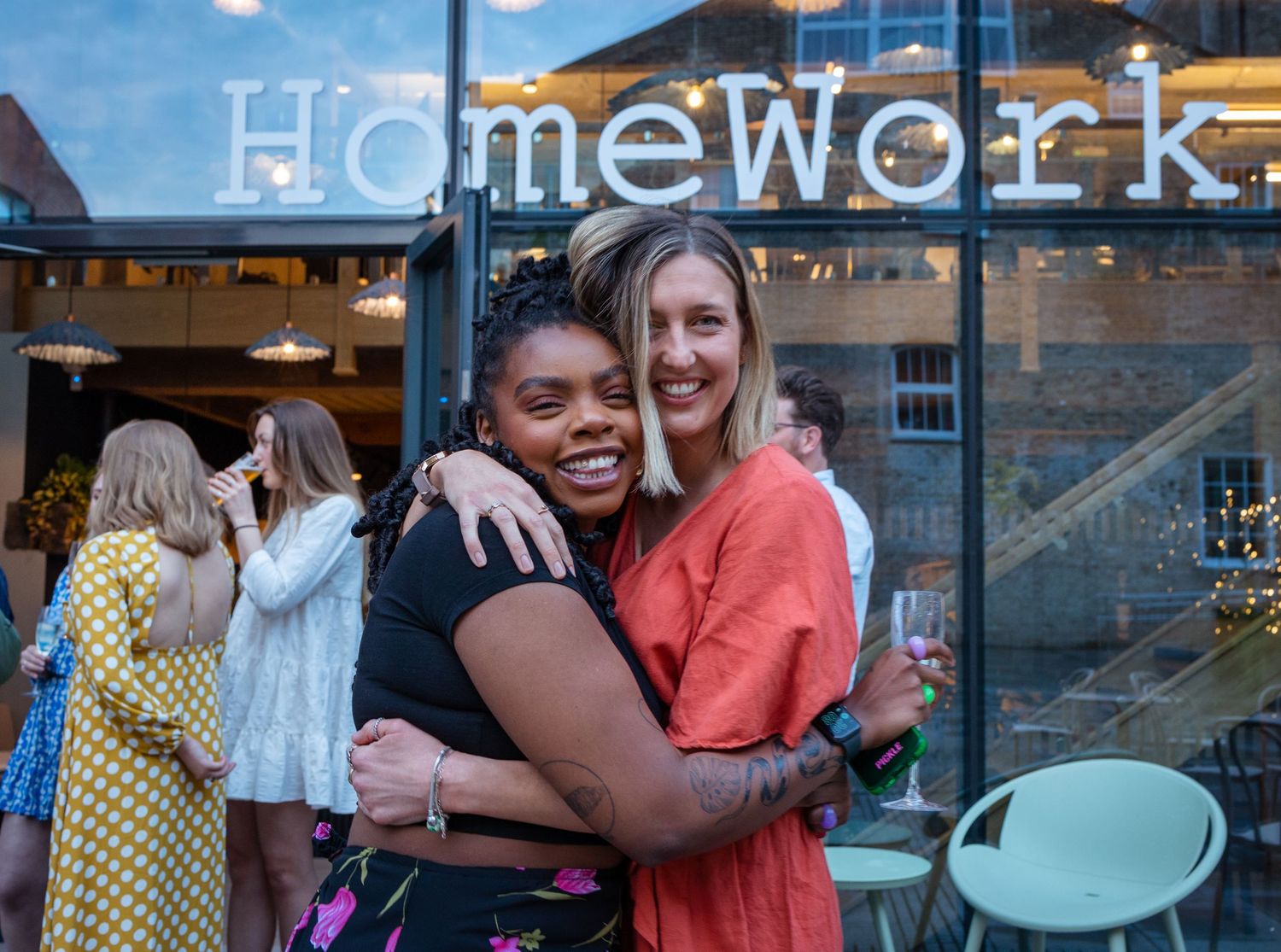 Two women share a warm hug outside HomeWork venue during a social gathering.