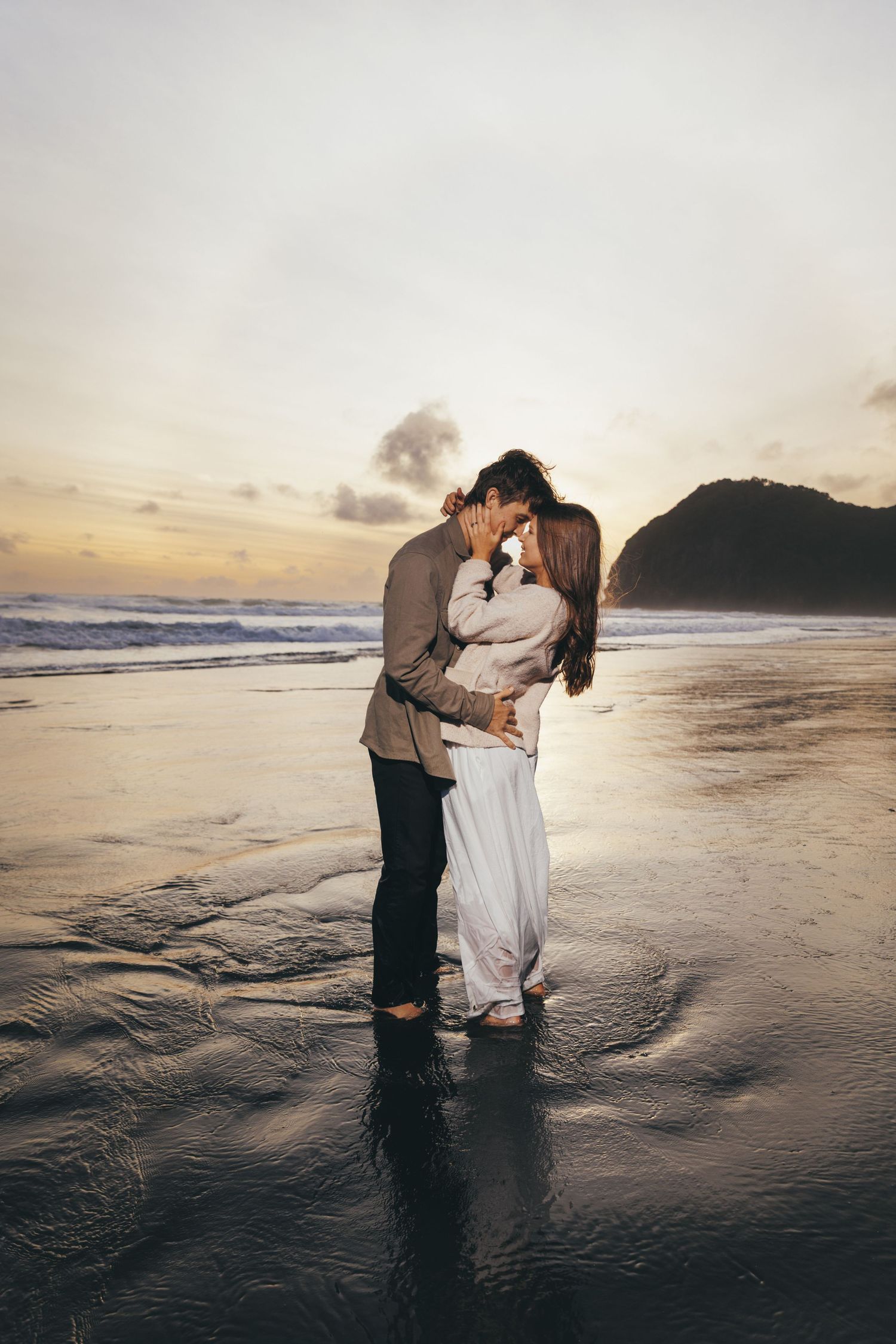 Romantic couple kissing on a reflective beach at stunning sunset.