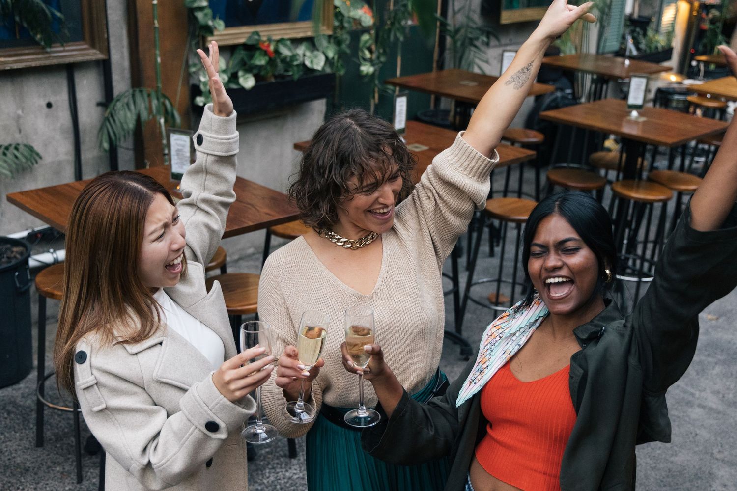 Three diverse women celebrating with champagne glasses raised in a restaurant.