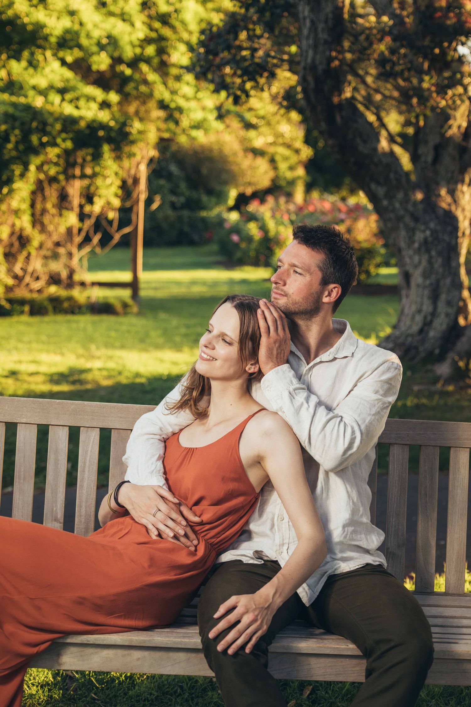 Romantic couple sitting on a wooden bench in a sunlit park, embracing tenderly.