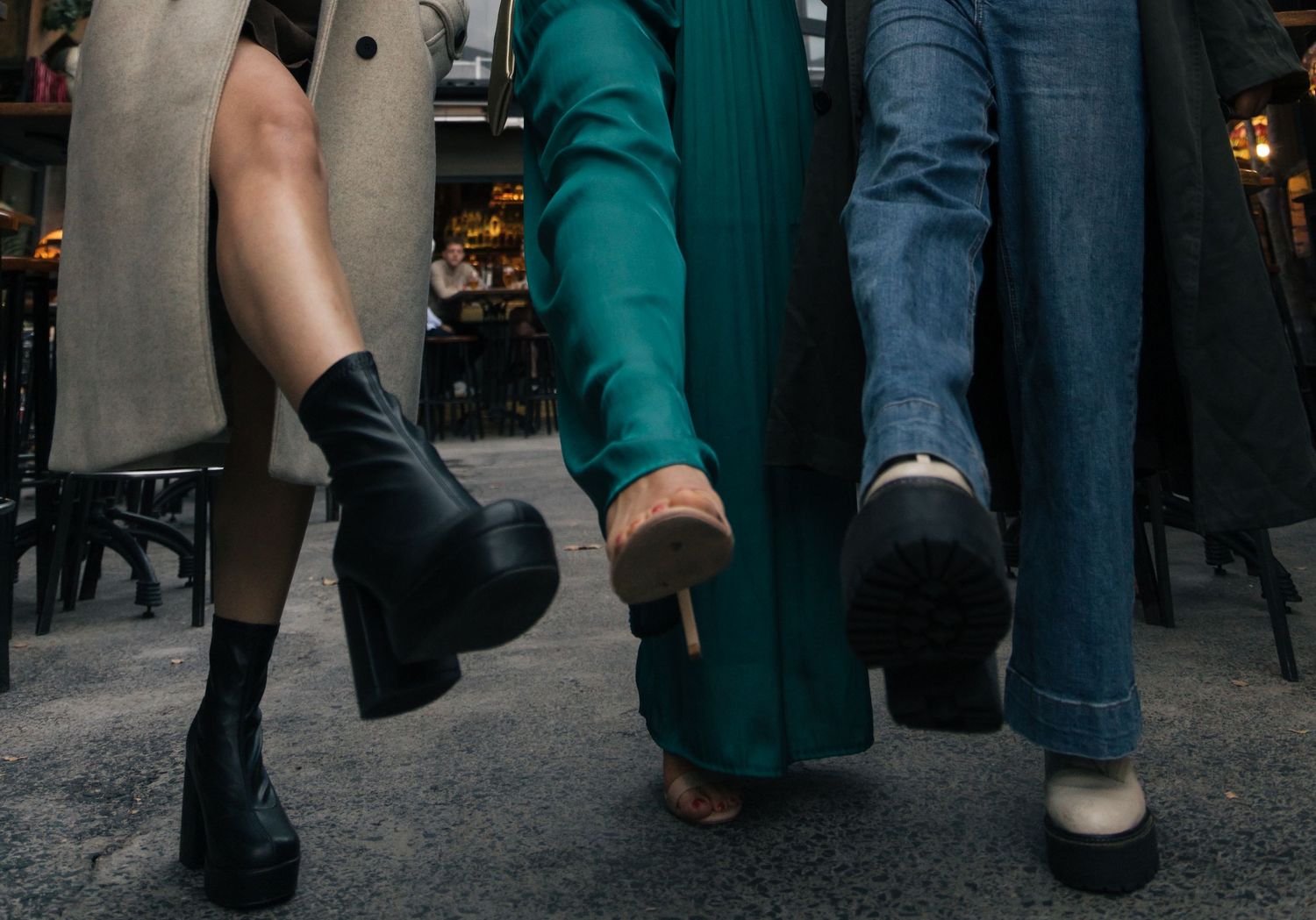 Three women walking in stylish platform boots and heels on a city street.