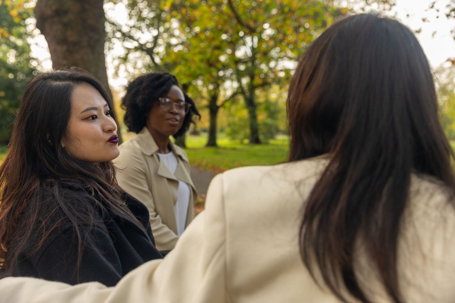 Three diverse women having a conversation outdoors in a park during autumn season.