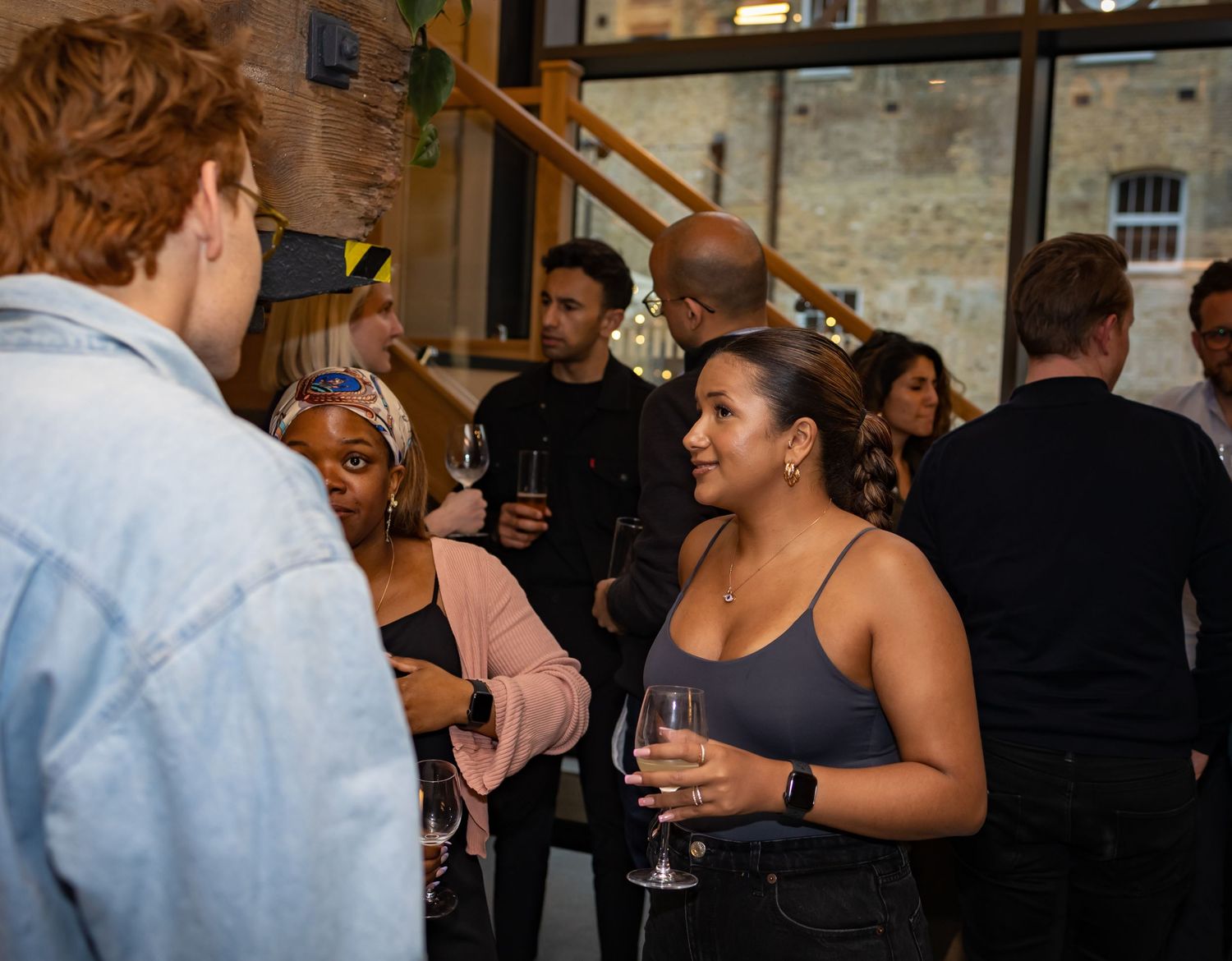 A woman holding a wine glass smiles during conversation at a vibrant indoor social event.