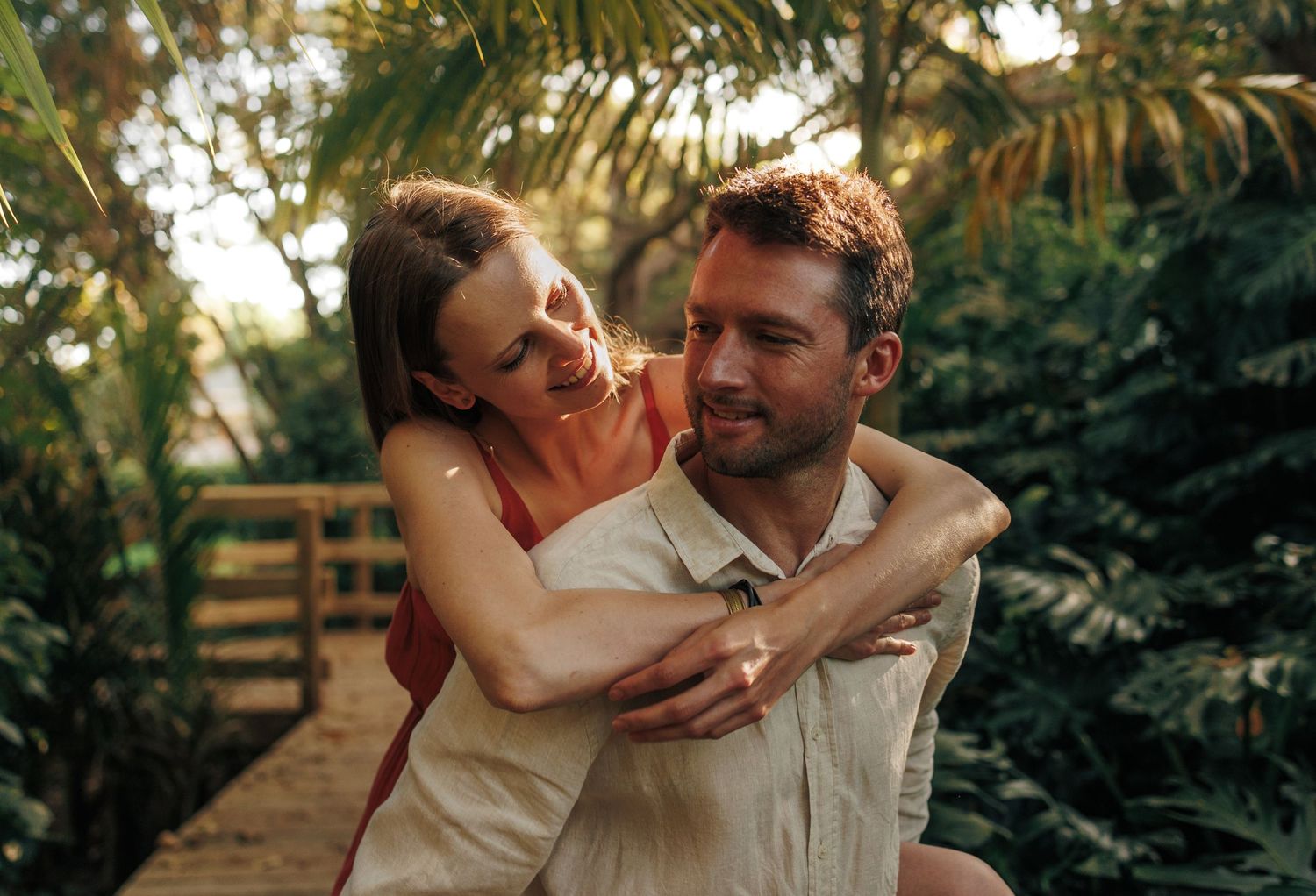 Happy couple laughing together on a wooden bridge surrounded by tropical greenery.