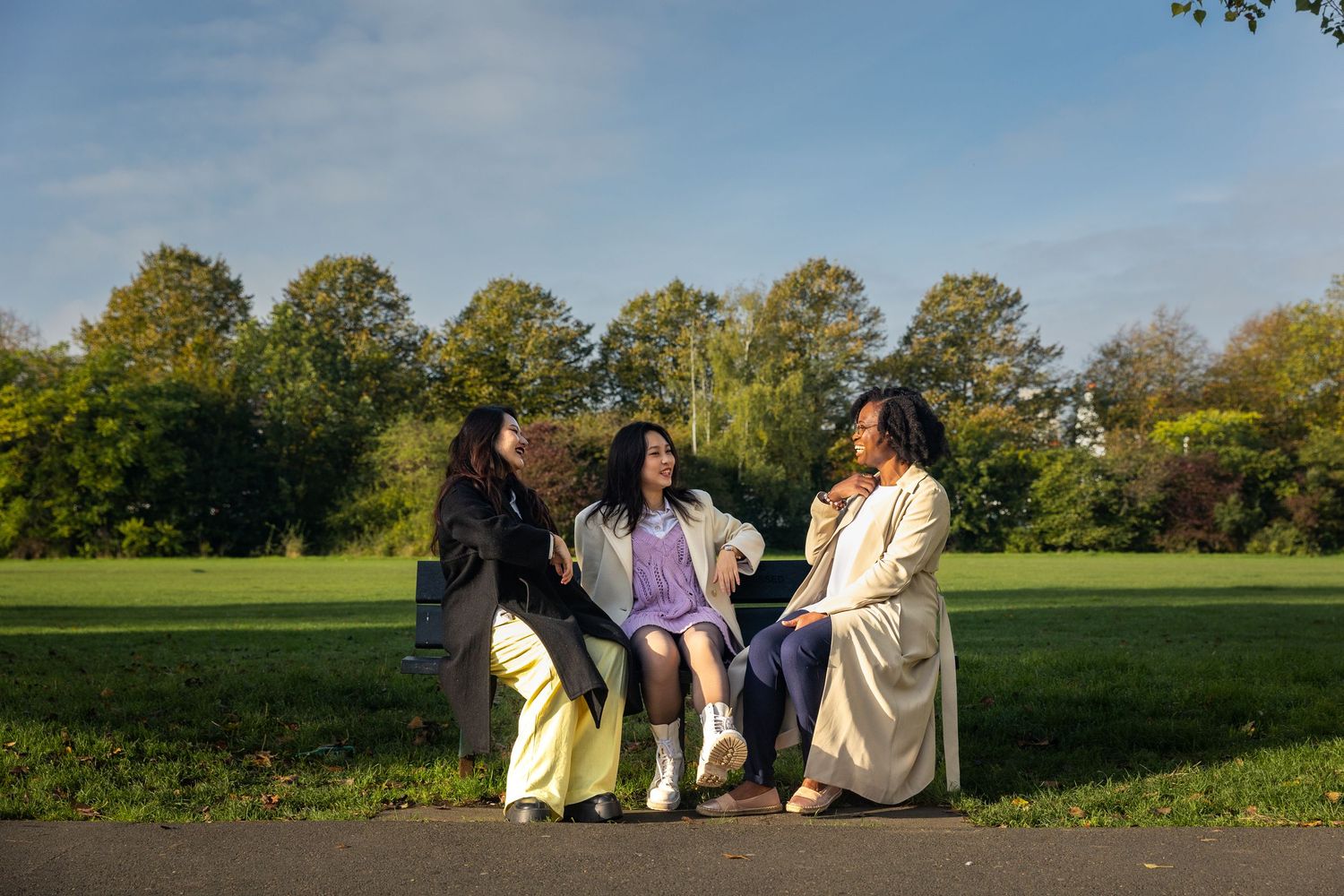 Three women relaxing and chatting together on a park bench on a bright sunny day.