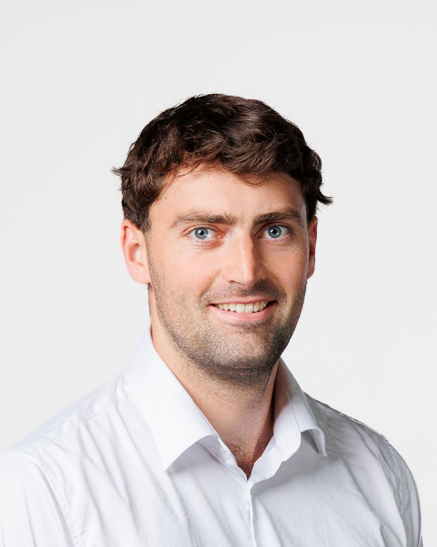 Professional headshot of a smiling man with brown hair and blue eyes wearing a white shirt.