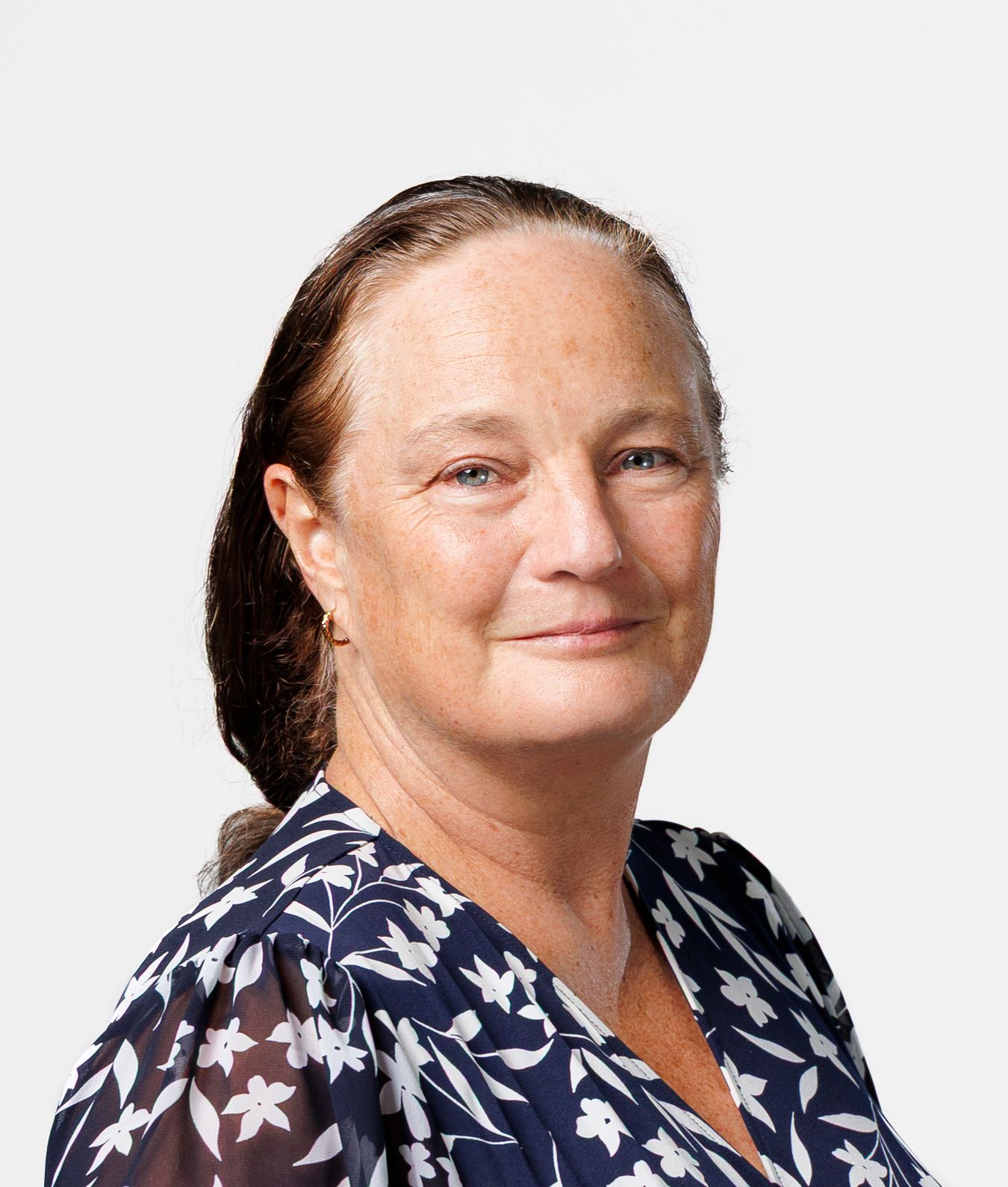 Professional headshot of a middle-aged woman with dark hair, wearing a navy floral blouse, smiling confidently.