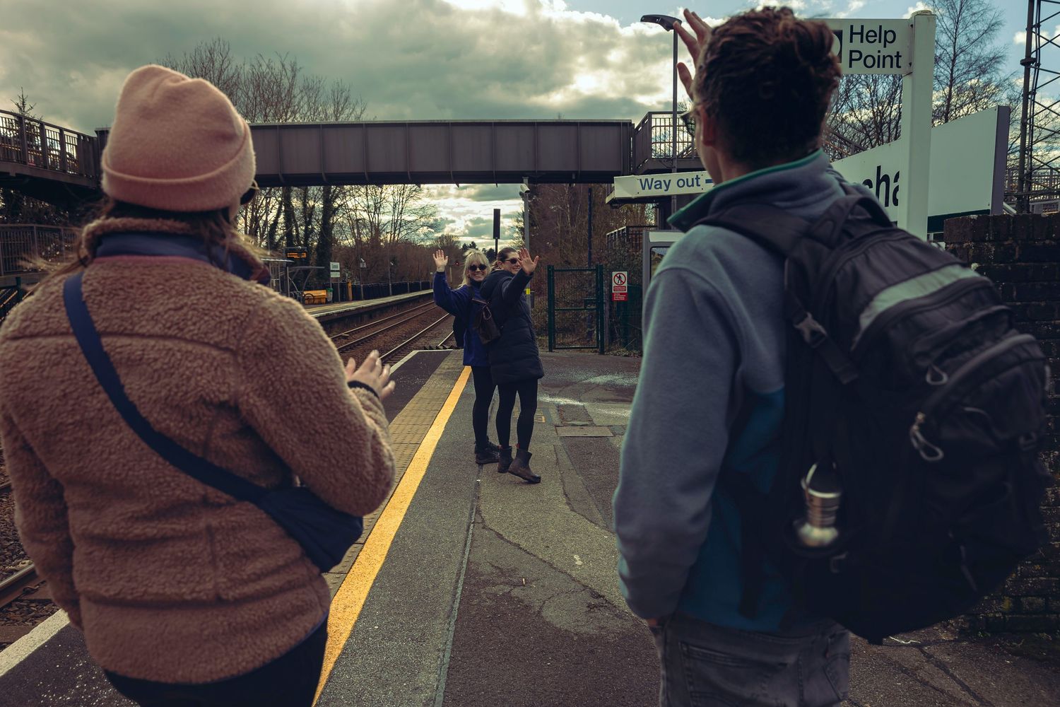 People waiting on a train platform in London with a Help Point sign visible in the background.