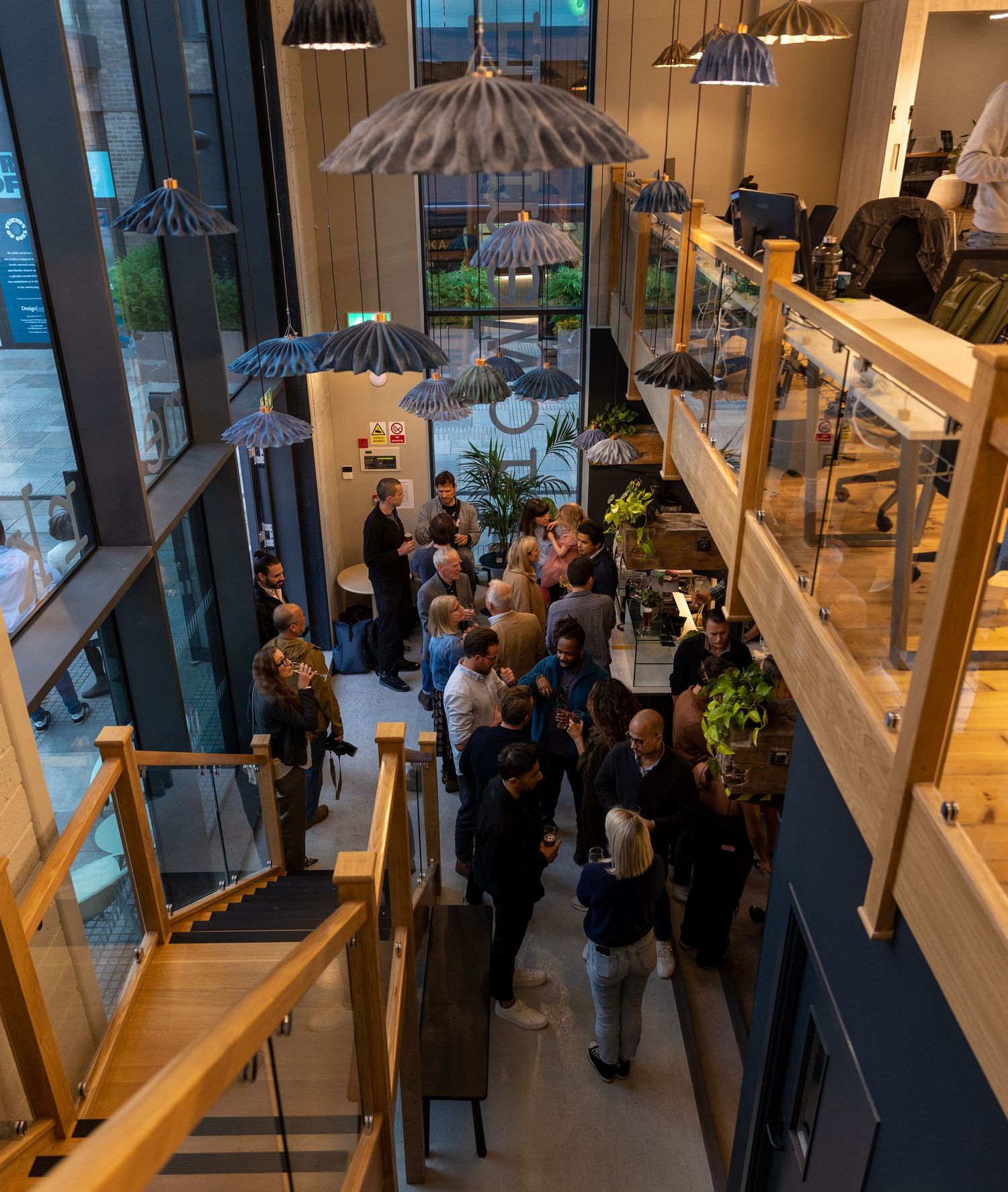 Aerial view of a busy networking event inside a modern multi-level venue with decorative pendant lights.