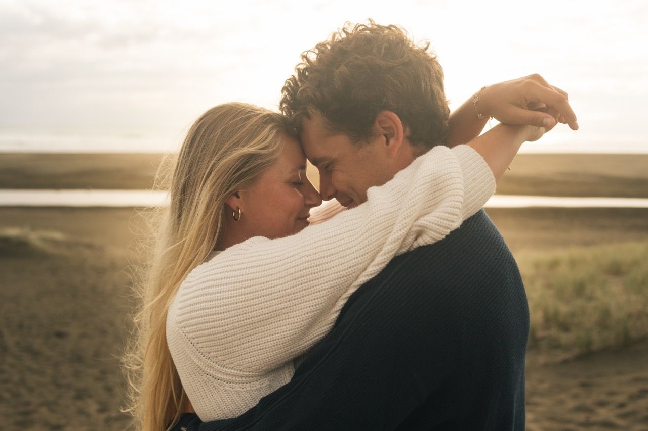 Romantic couple embracing on a beach at sunset, sharing a tender forehead-to-forehead moment.