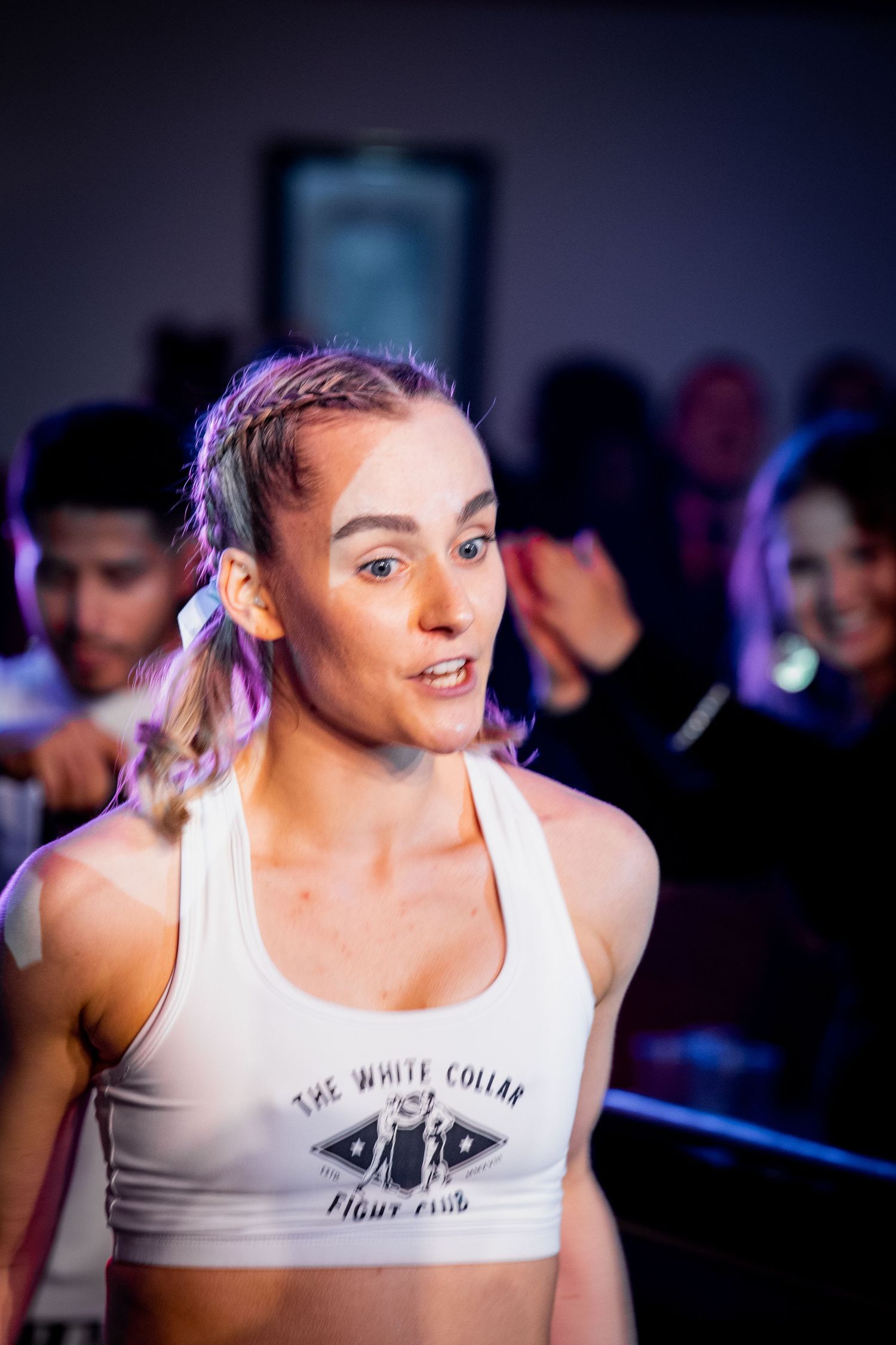 A female boxer in a White Collar Fight Club sports bra stands ringside at a boxing event.