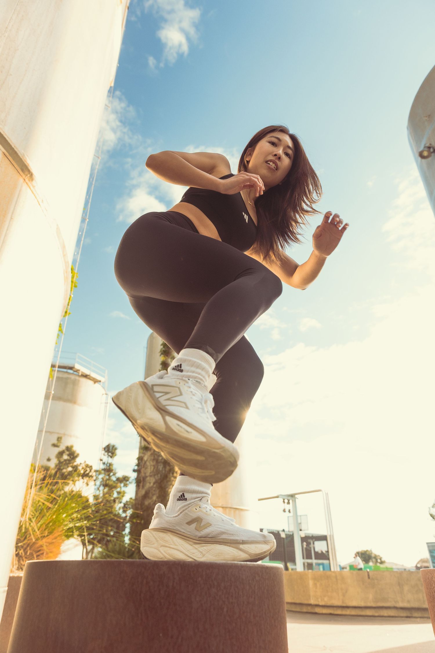 Athletic woman in black workout set jumping on an outdoor platform in an urban environment.