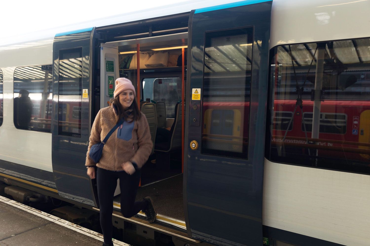 Young woman in a pink beanie stepping off a train onto a station platform.