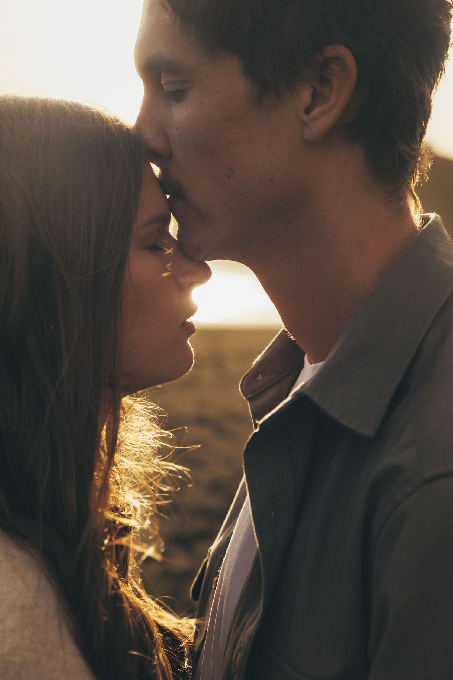 A couple shares a tender moment, foreheads touching at golden sunset.