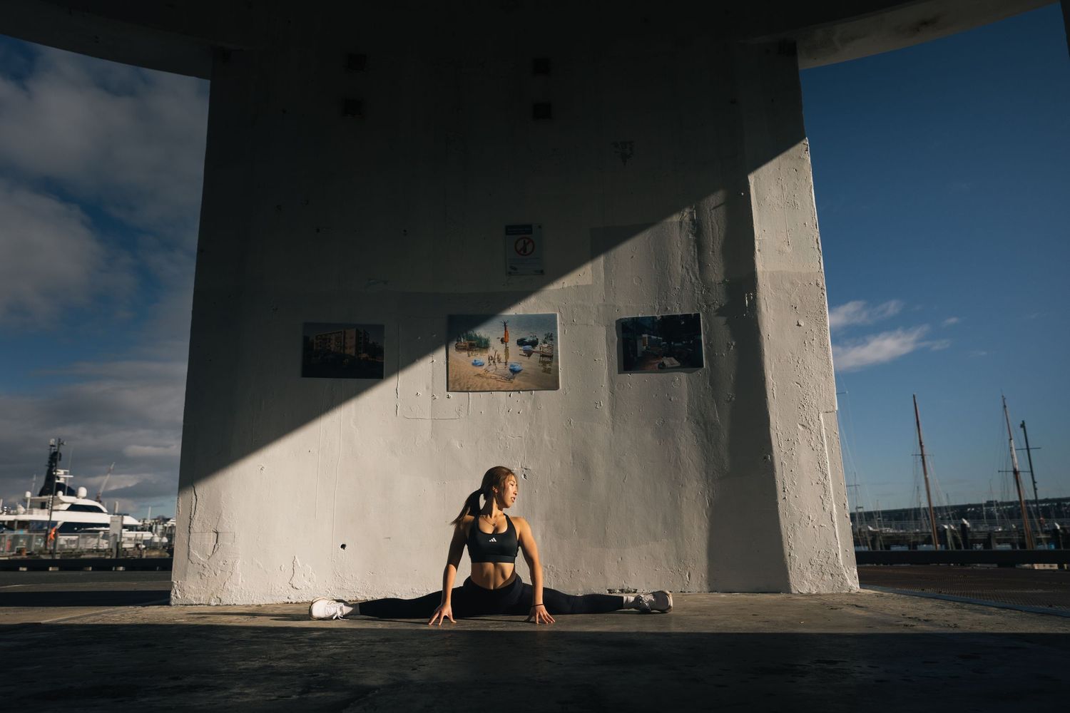 Athletic woman in black sportswear doing a low lunge stretch outdoors near a concrete wall.