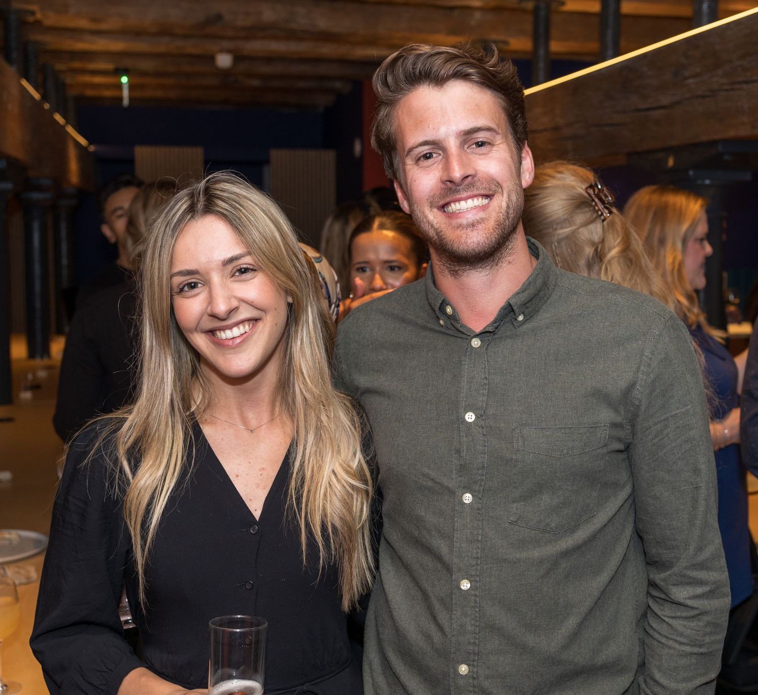 Smiling couple poses together at a lively indoor social event.