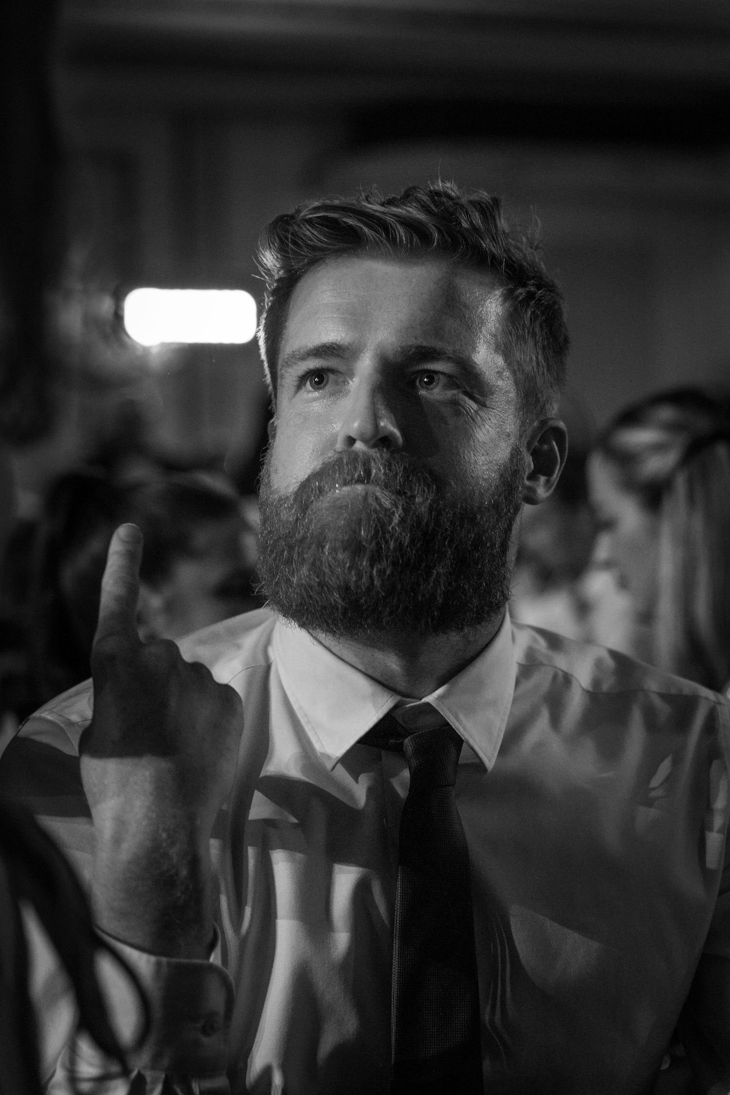 Black and white portrait of bearded man in shirt and tie looking upward at event.