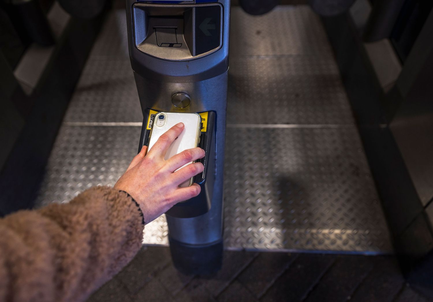 A hand tapping a contactless card on a transit turnstile payment terminal.