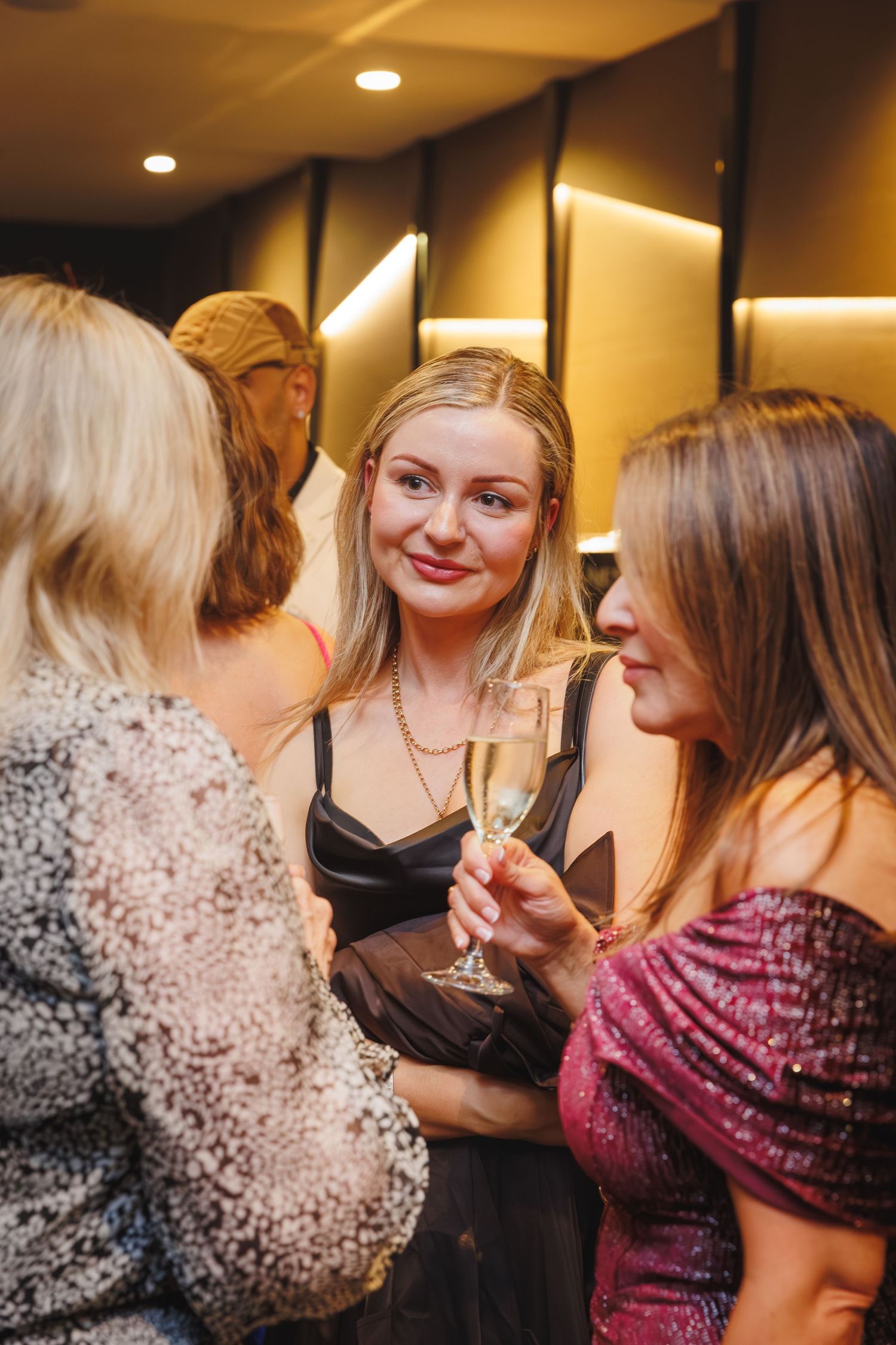 Three women socializing at an elegant party, one holding a champagne glass wearing a black dress.