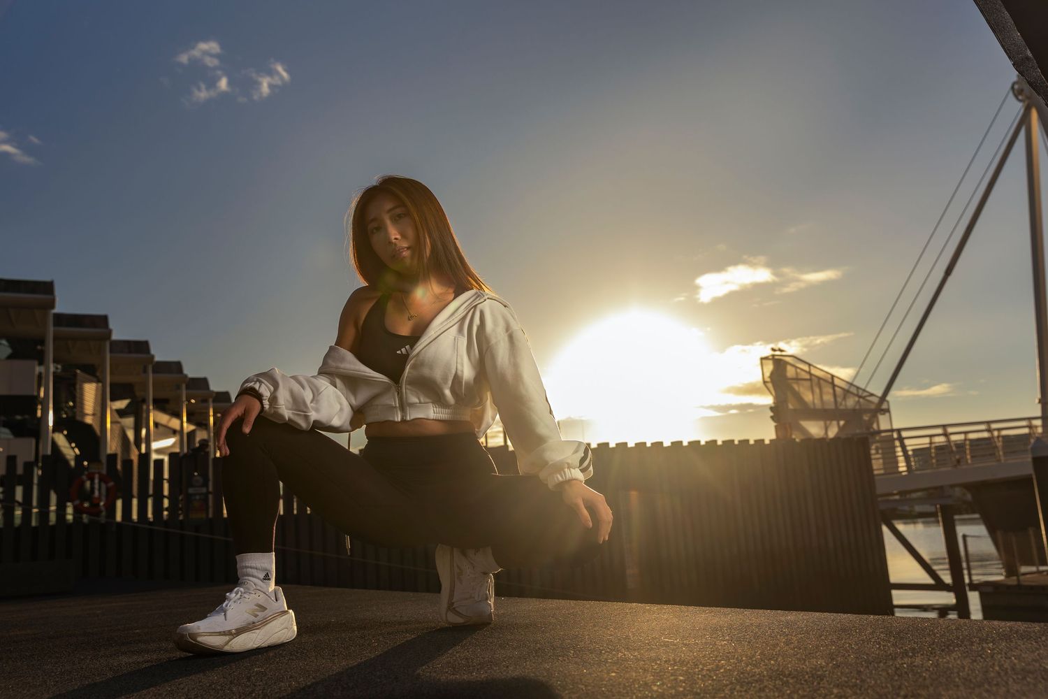 Young woman in white jacket sitting outdoors at sunset with golden light behind her.