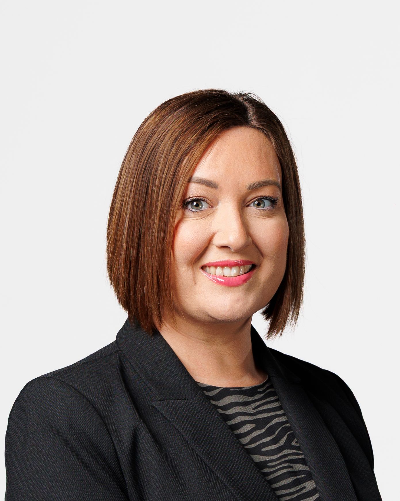 Professional headshot of a smiling woman with auburn bob haircut wearing a black blazer against a white background.