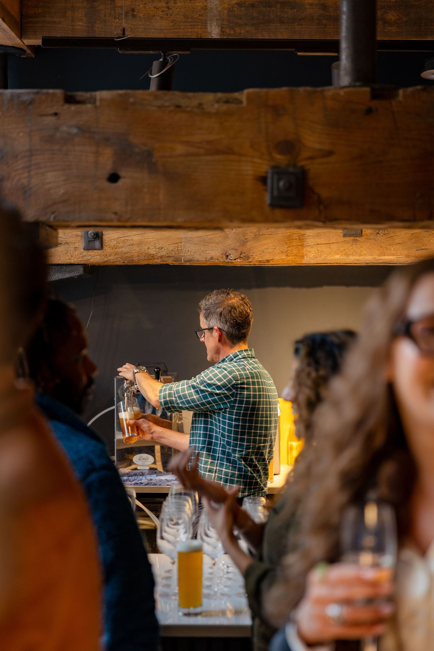 Bartender pouring a draft beer at a rustic wooden bar during a busy social event.
