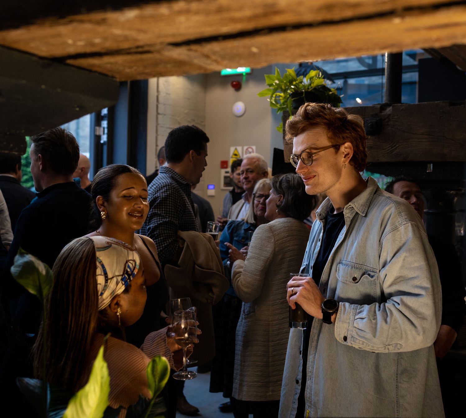 A young man and woman laugh together while holding drinks at a busy social event.