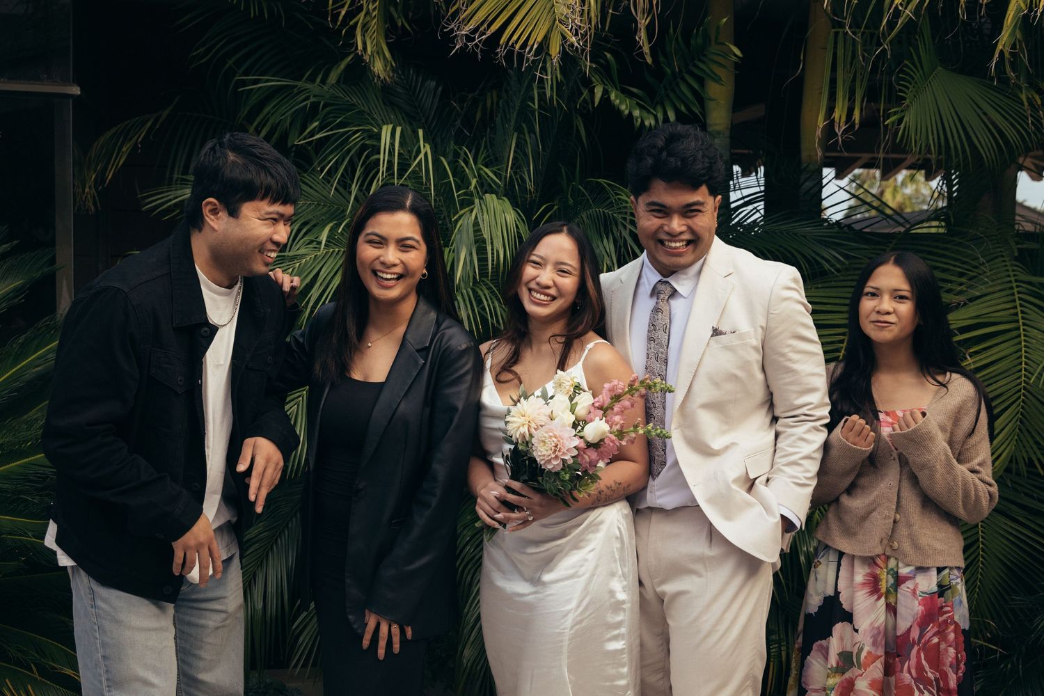 Bride and groom celebrate with three guests amid lush tropical greenery at their wedding.