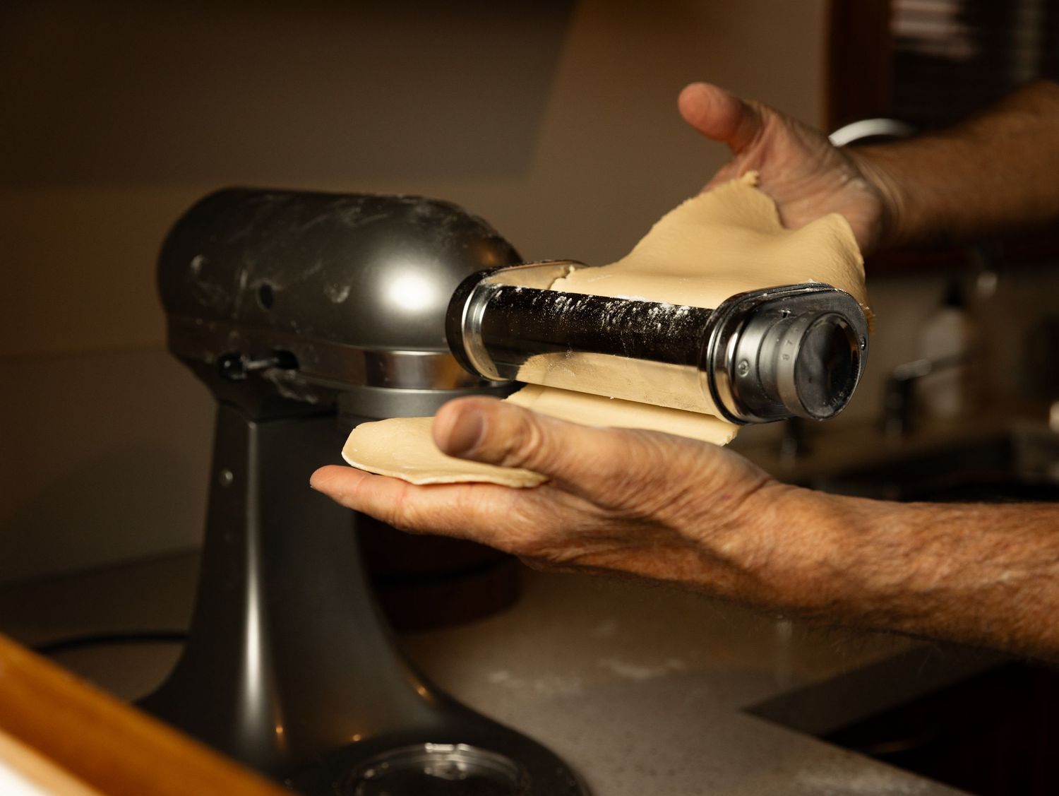 Close-up of hands attaching a pasta roller attachment to a KitchenAid stand mixer.