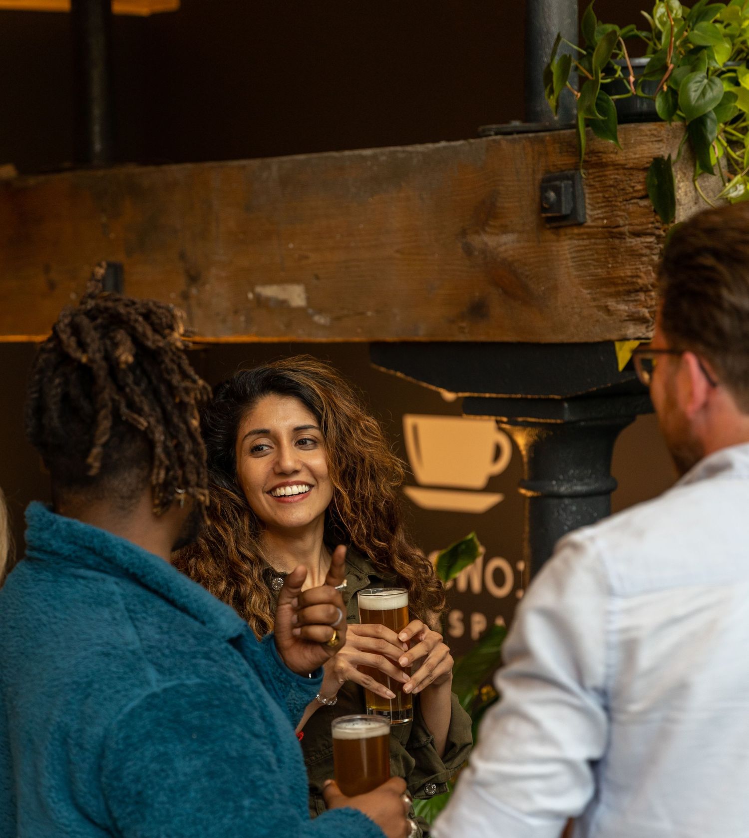 Three friends laughing and clinking beer glasses at a rustic indoor bar event.