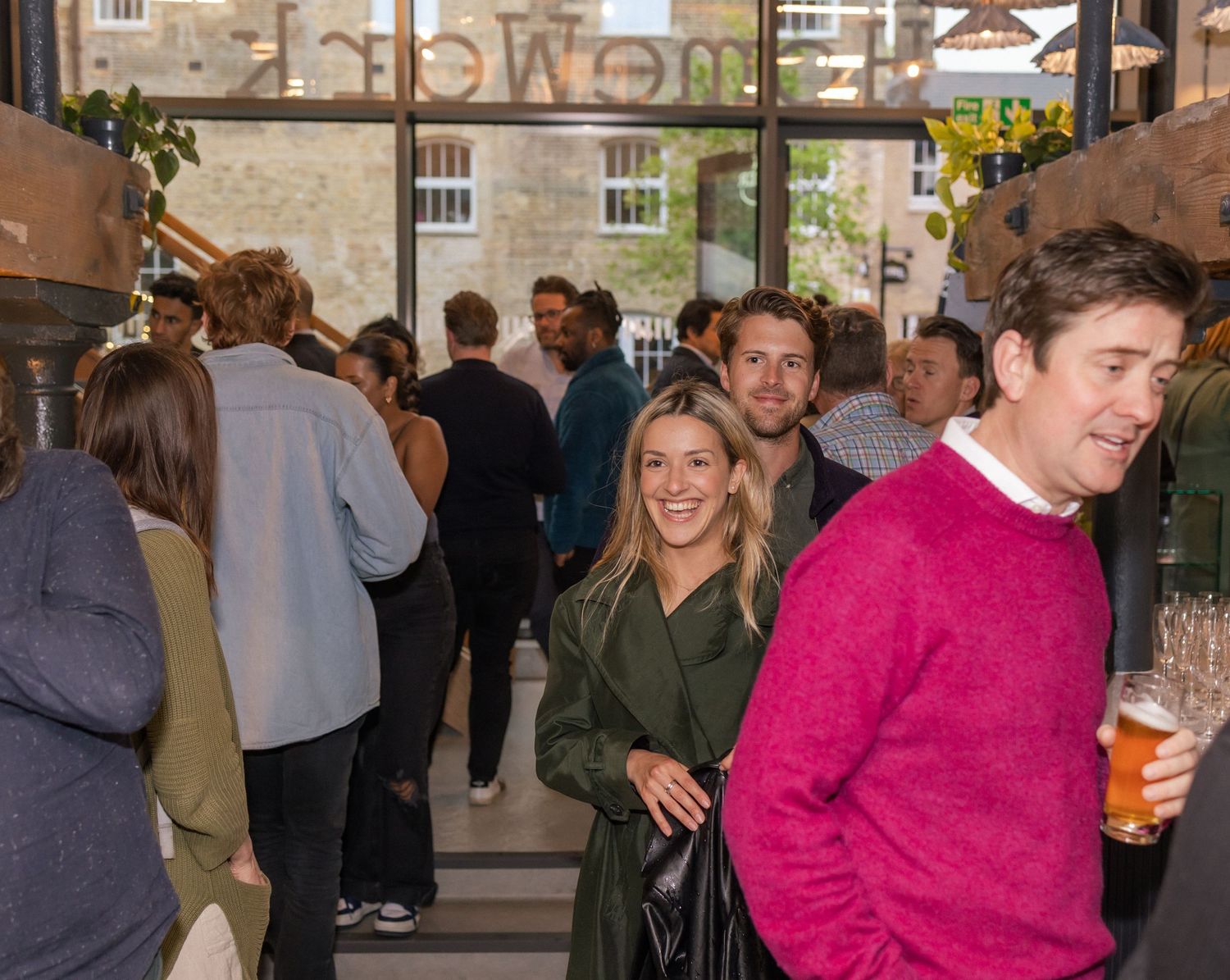 A crowd of smiling professionals mingle with drinks at a busy indoor networking event.