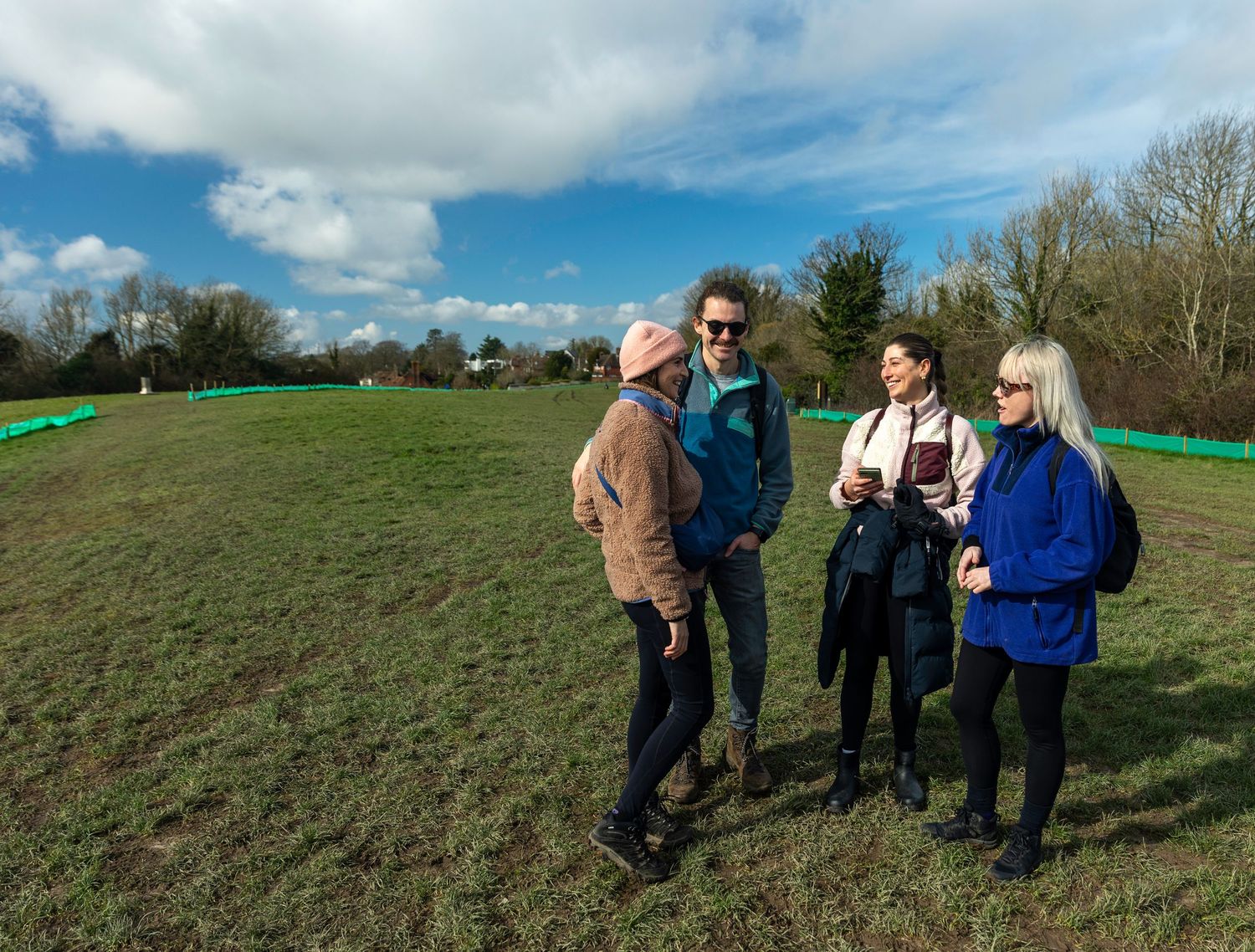 Four people having a conversation in an open green field under a blue sky.