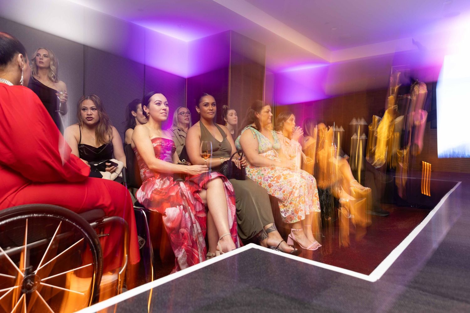 Diverse audience seated along a illuminated fashion runway at an elegant indoor event.
