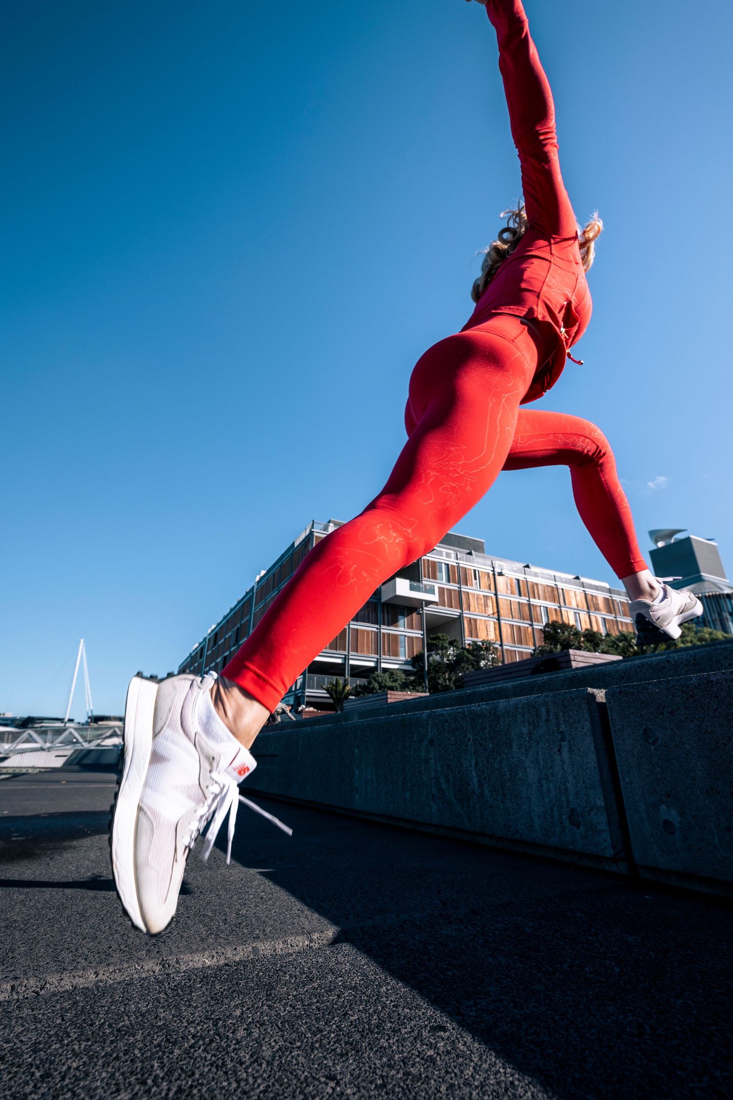 Low angle view of woman in red outfit jumping against a clear blue urban sky.