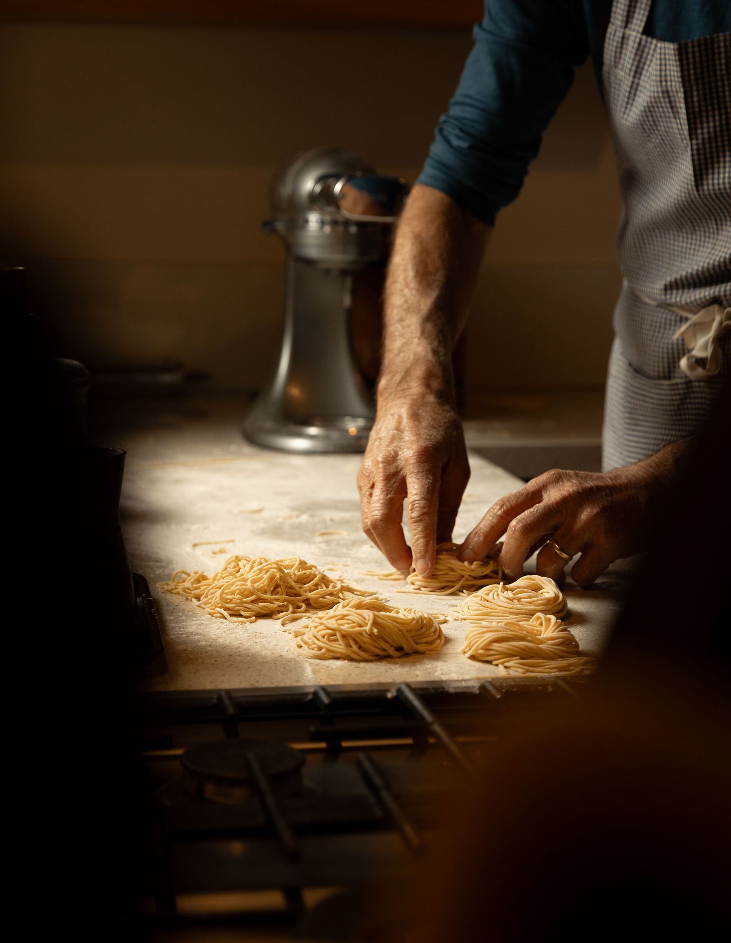 Person in apron arranging fresh spaghetti nests on a floured baking tray.