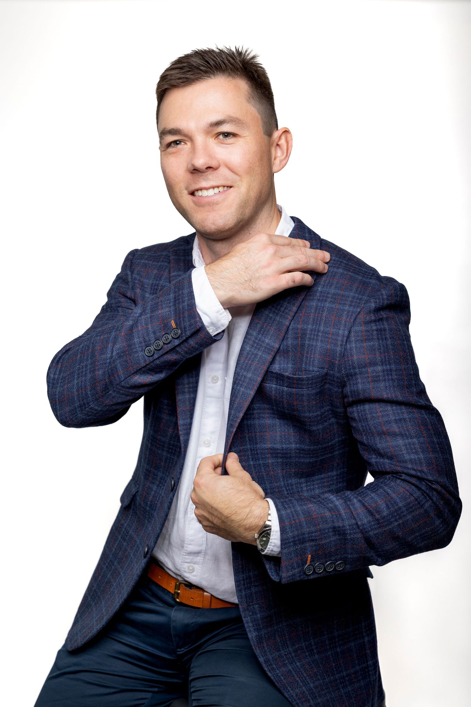 Smiling man in navy plaid blazer and white shirt posing confidently against white background.