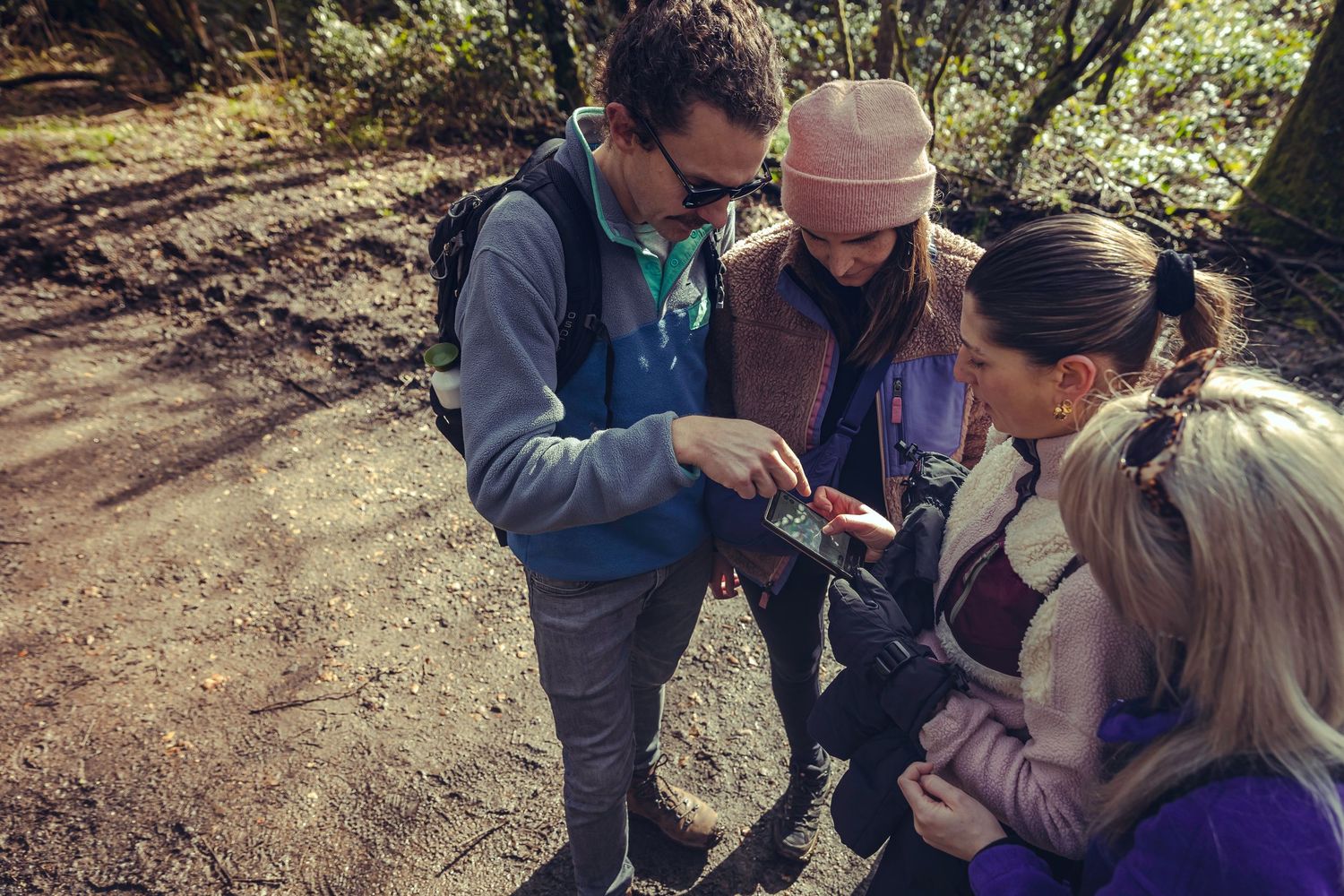 Four hikers gathered on a forest trail examining a small object together.