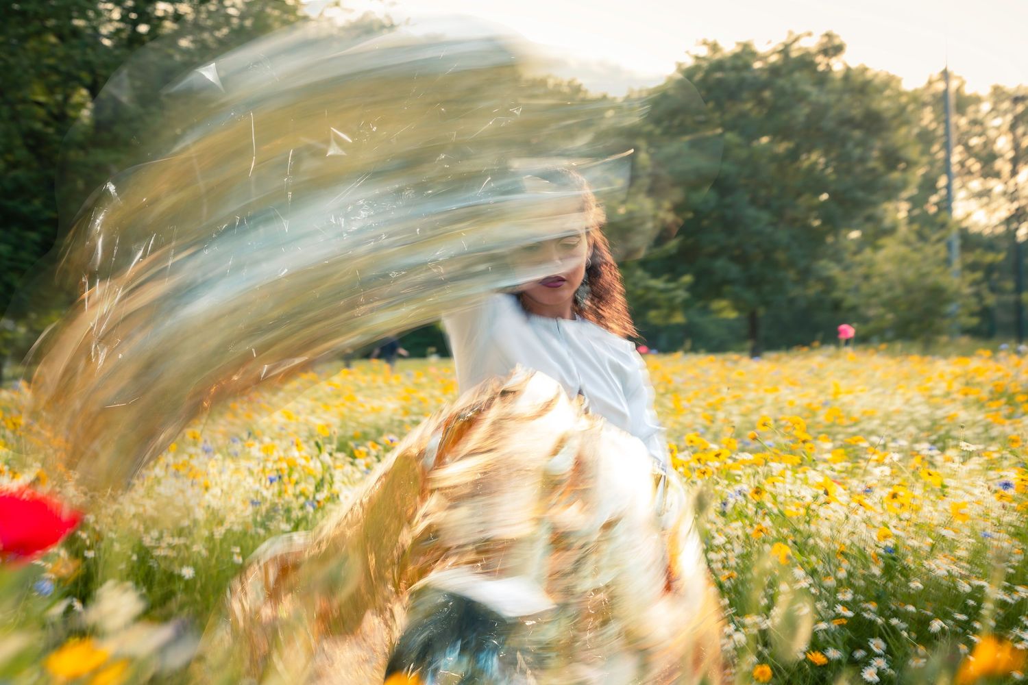Woman spinning in white outfit in sunny wildflower field creating motion blur effect.