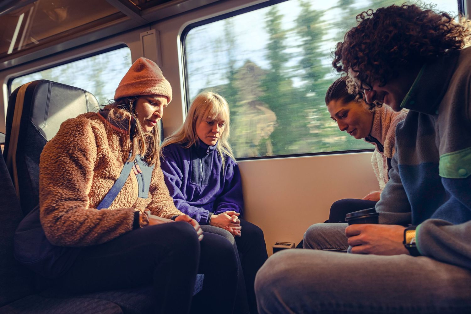 Three young friends looking at a smartphone together while riding on a train.