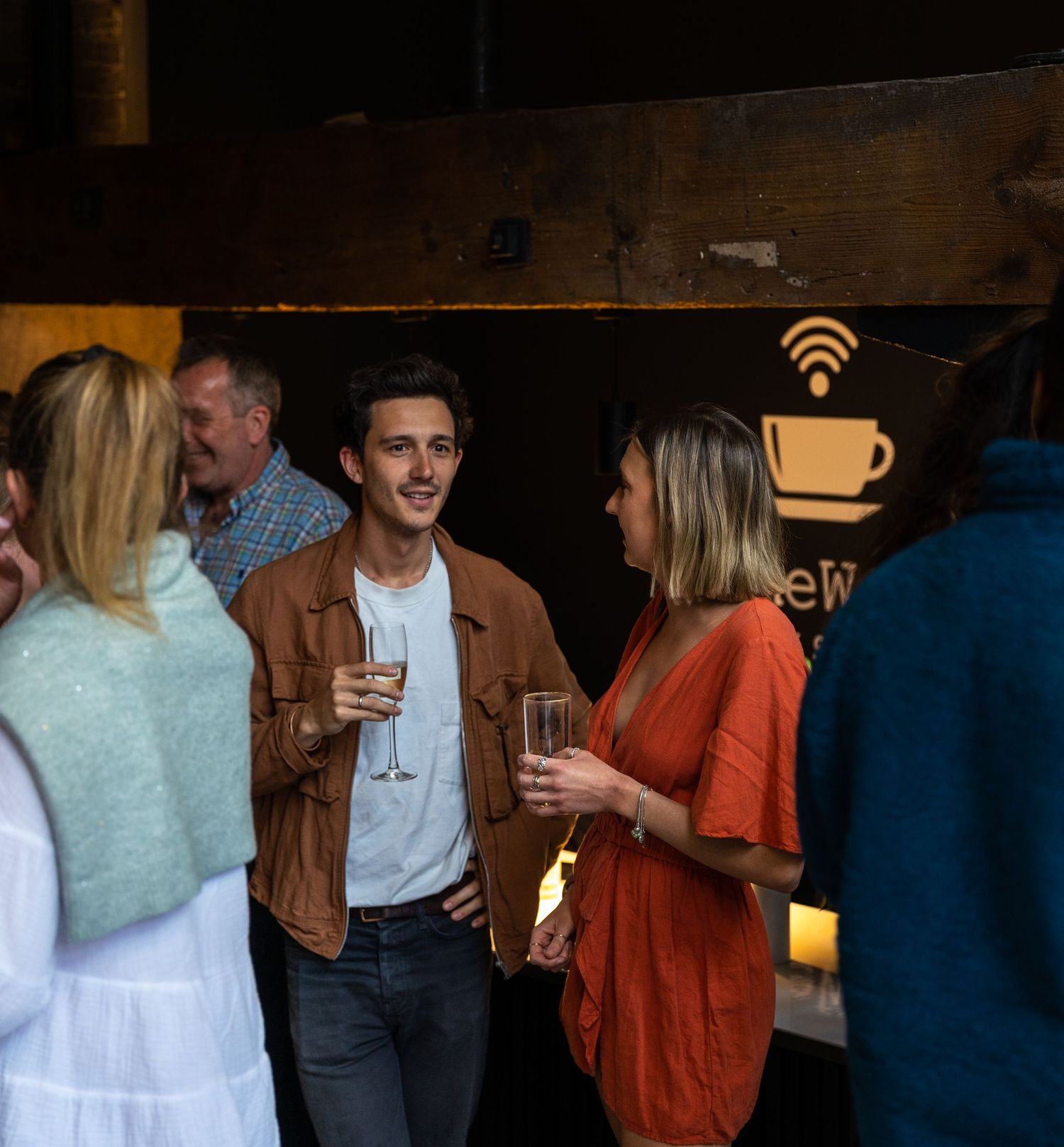 Group of young adults socializing with drinks at a cozy indoor evening gathering.