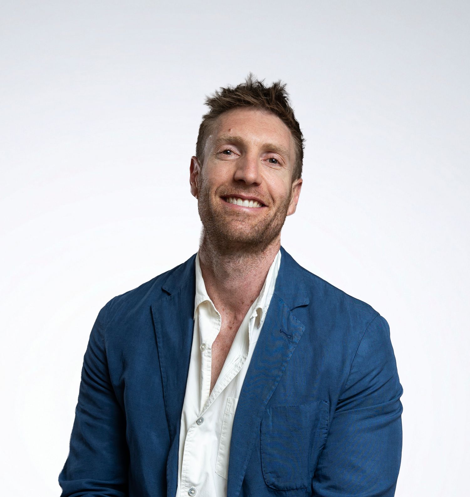 Cheerful man in blue linen blazer smiling broadly against a white background.