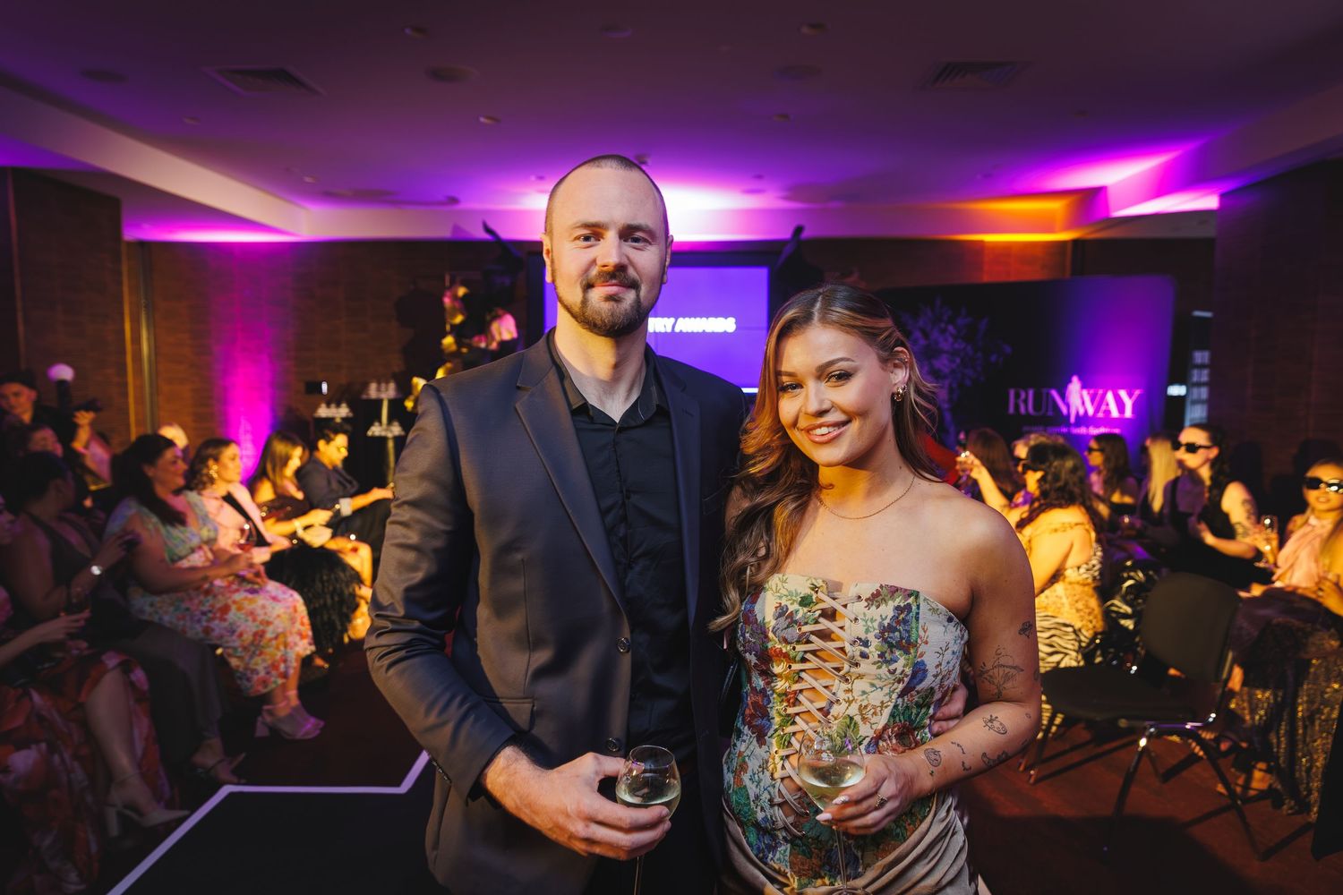 Couple posing together at a formal event, man in black suit, woman in gold strapless gown.