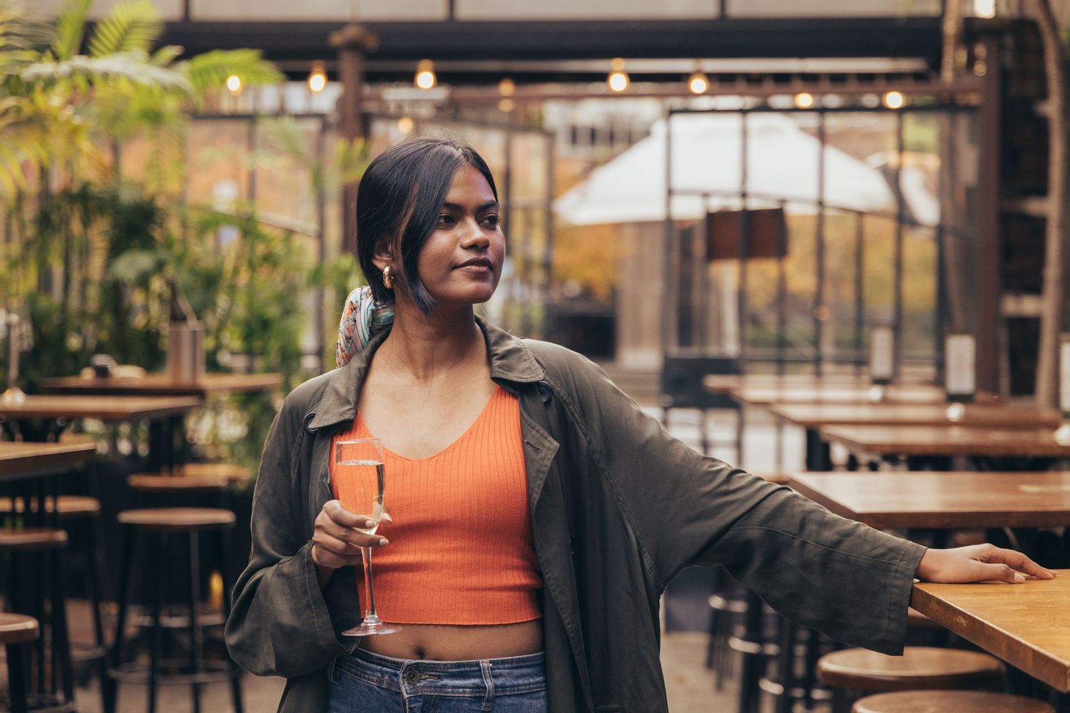 Young woman holding a champagne glass in a stylish outdoor restaurant setting.