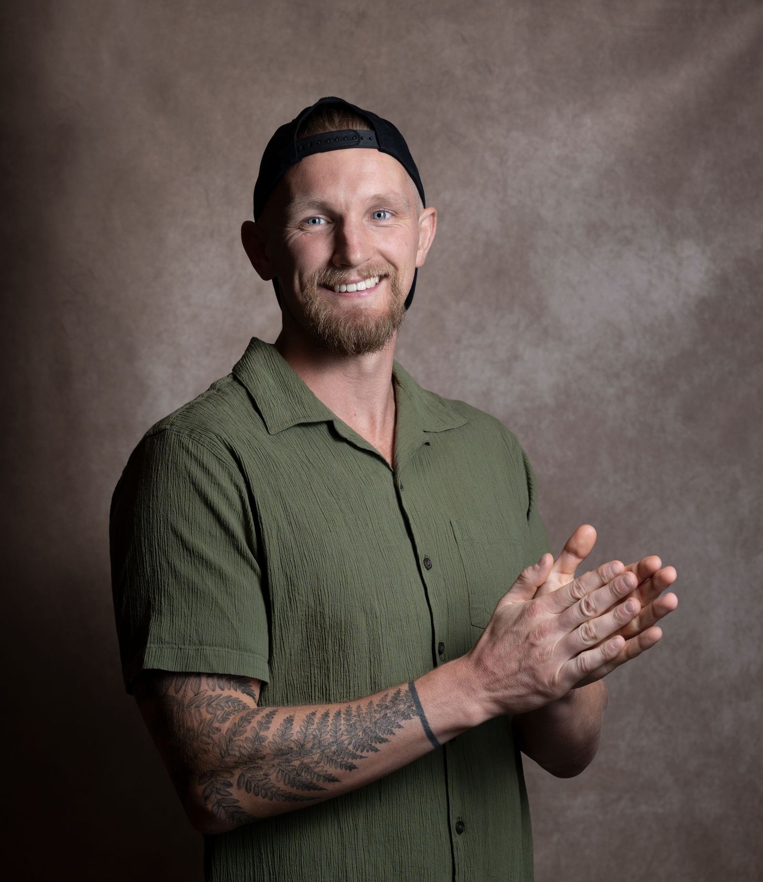 Tattooed man in green shirt clapping hands wearing backwards cap in studio.