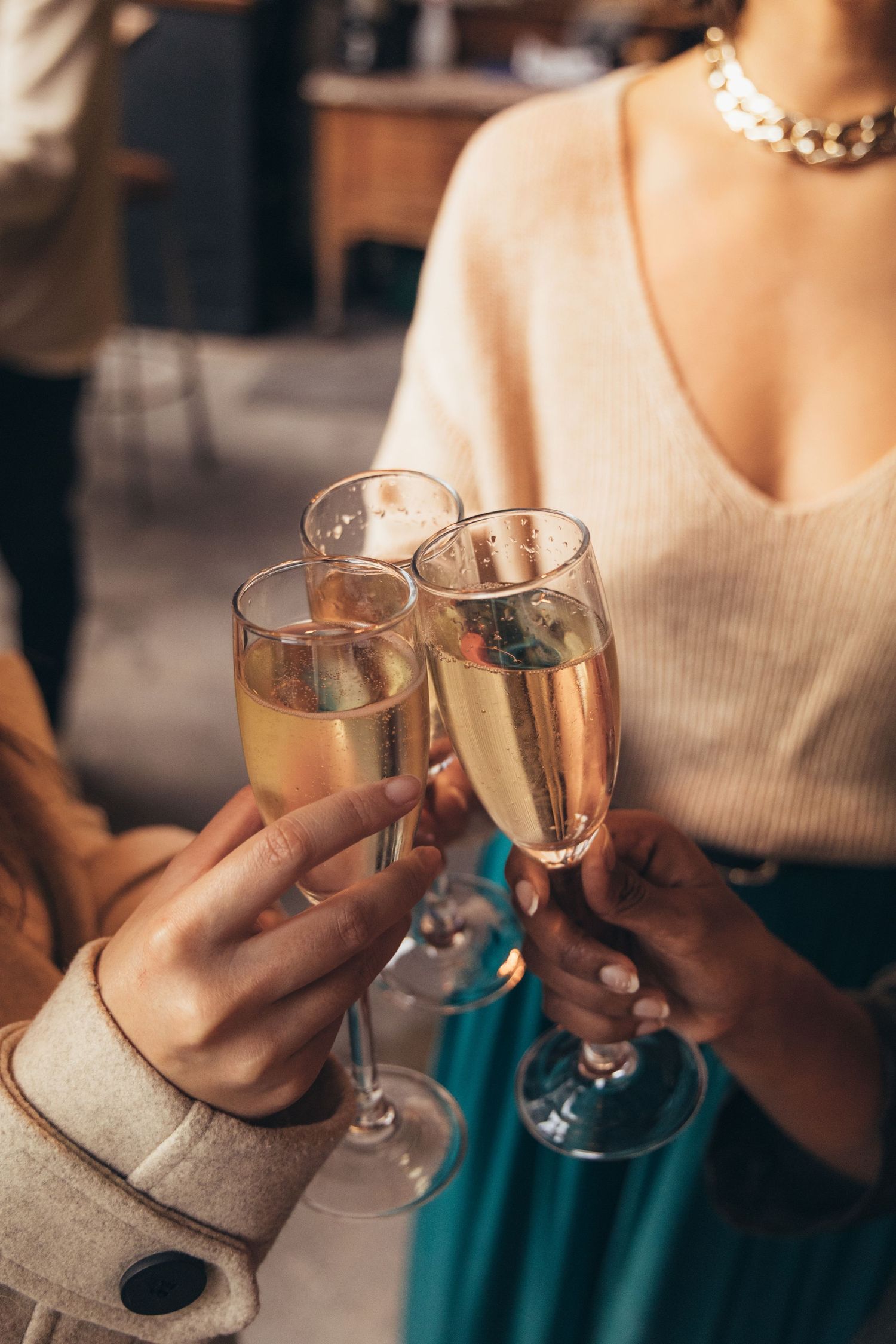 Close-up of three people clinking champagne flutes together in a celebratory toast indoors.