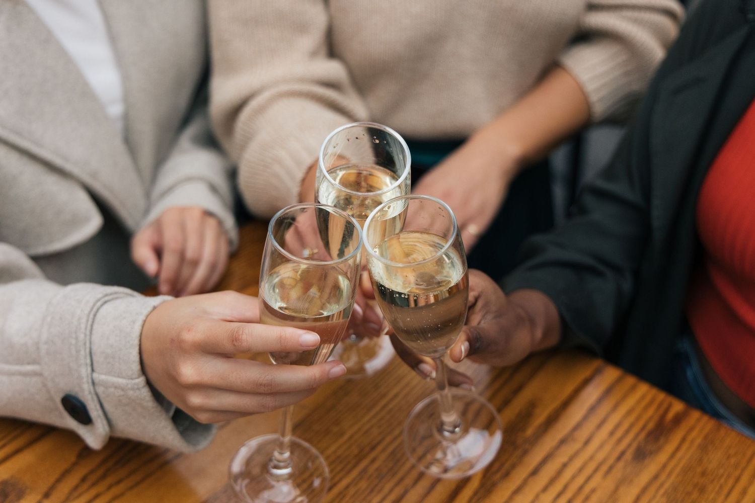 Three women clinking wine glasses together at a wooden table in a celebratory toast.