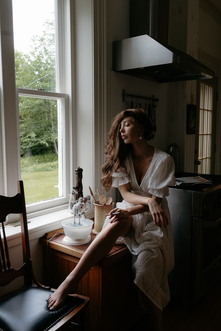 Woman in white dress sitting on kitchen counter by window in natural light.