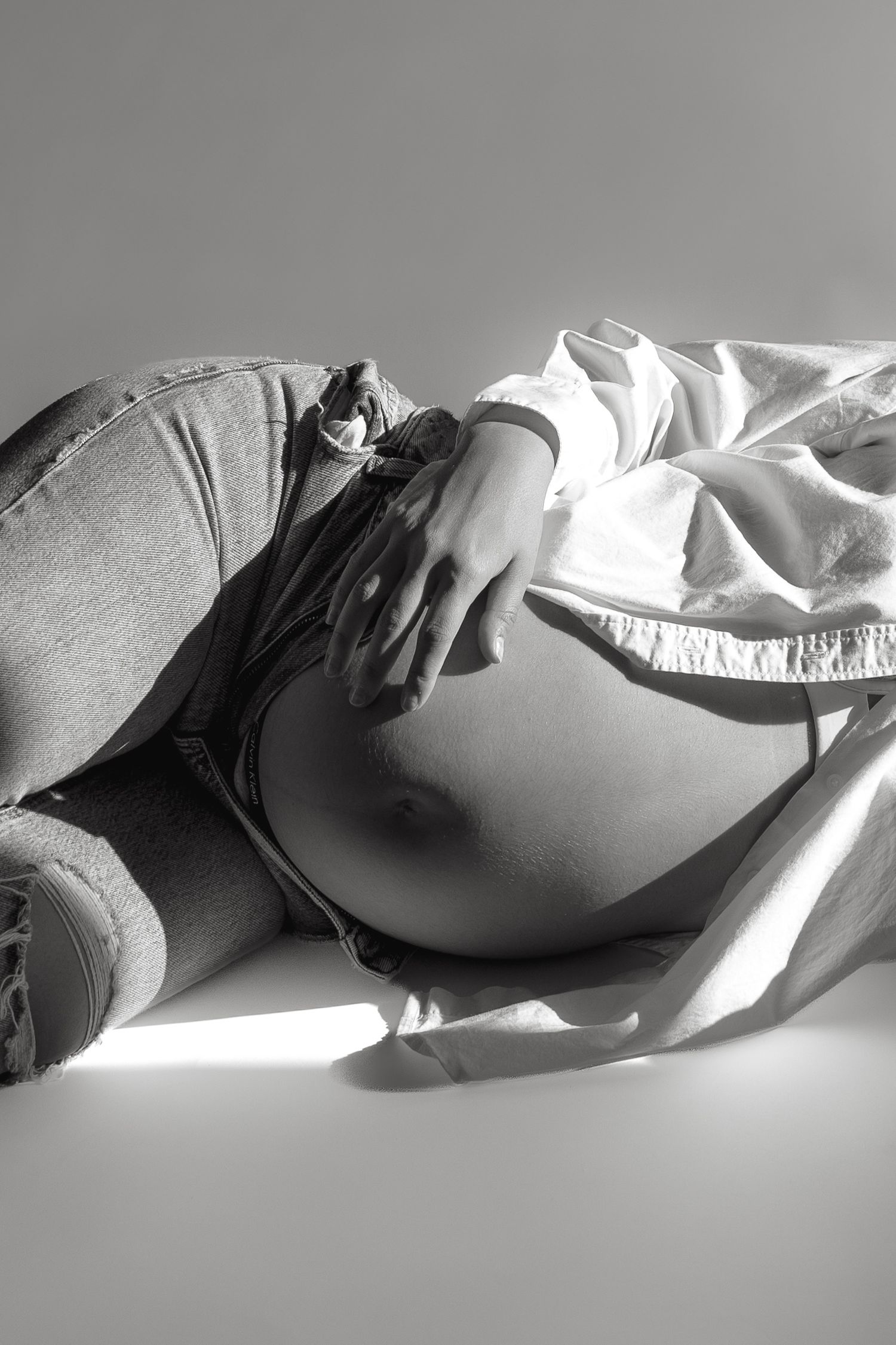 Black and white photo of a pregnant woman lying down, gently cradling her bare baby bump.